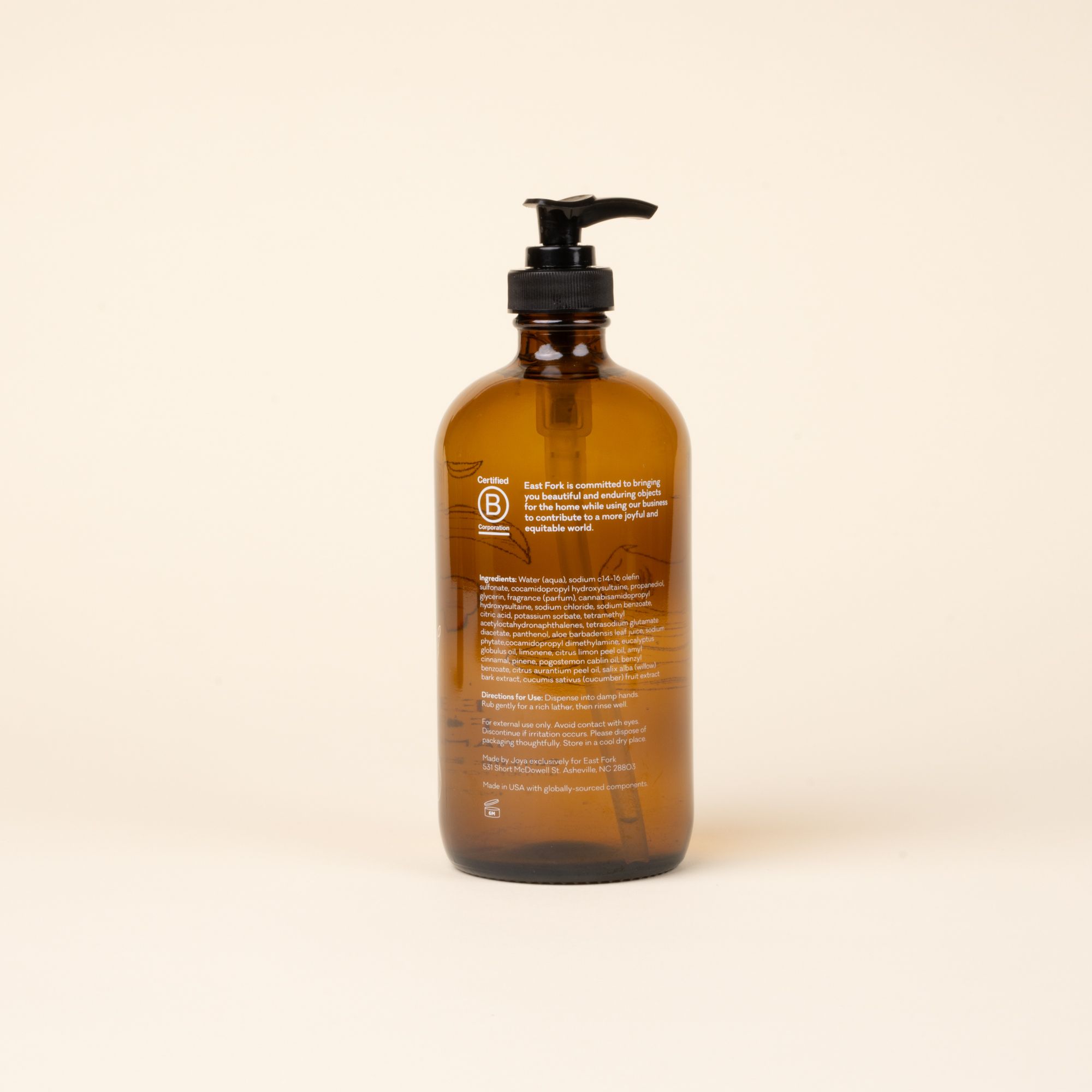 The back of an amber glass pump bottle of East Fork hand soap with ingredients, centered against a light neutral background.