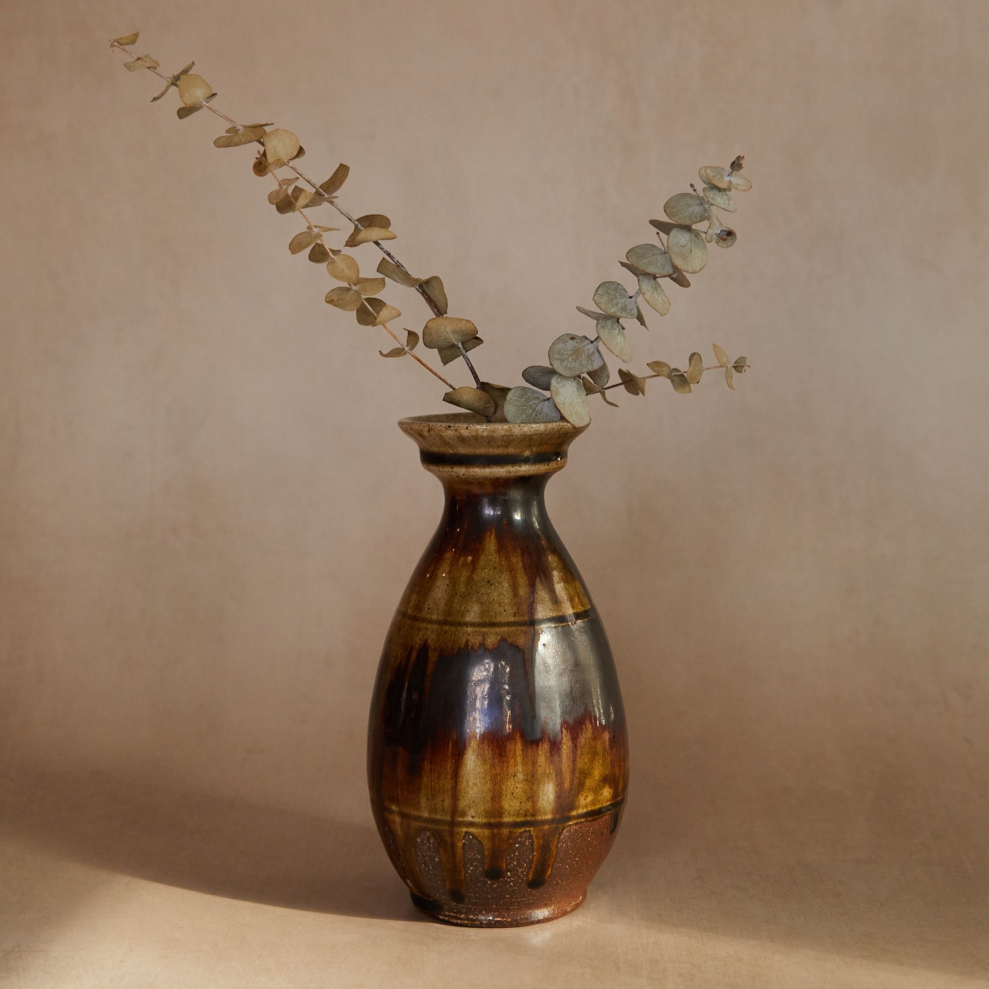 Large vase with a brown drippy glaze filled with dried eucalyptus 