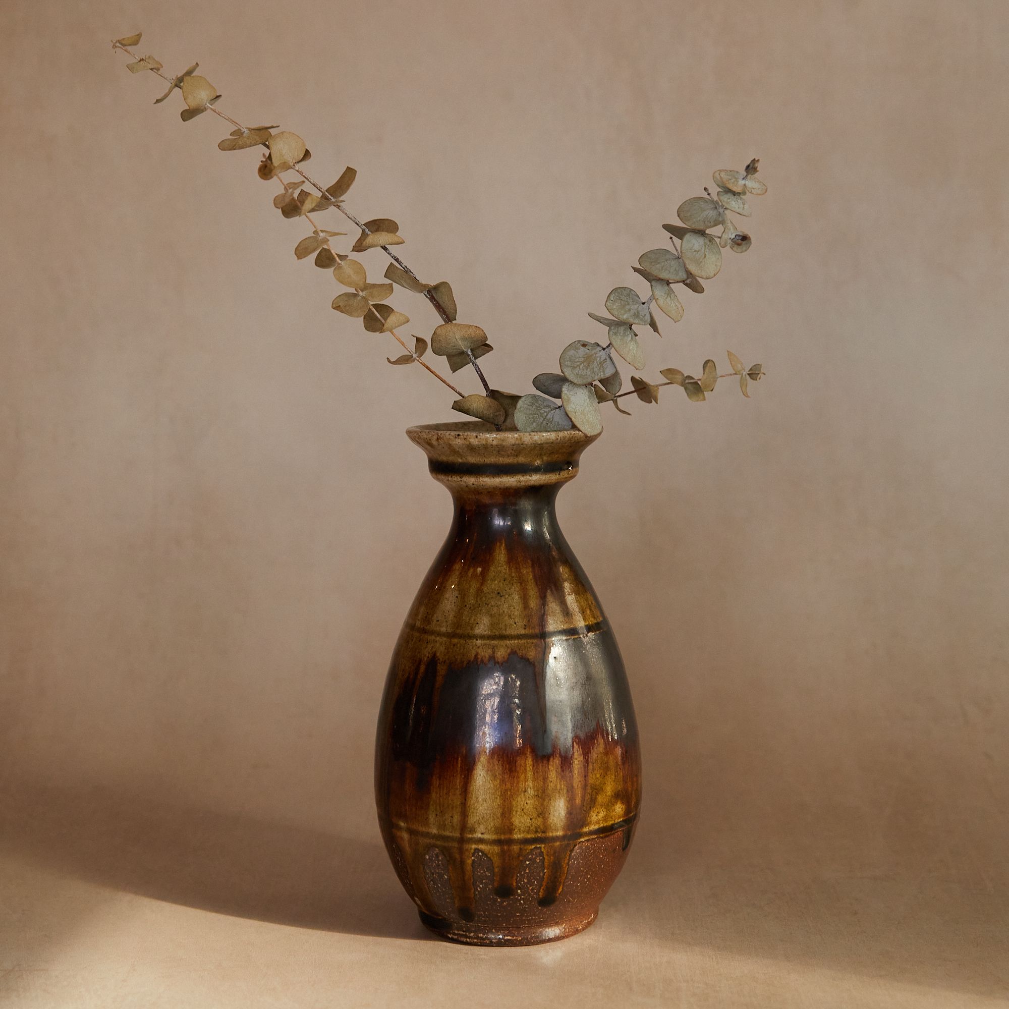 Large vase with a brown drippy glaze filled with dried eucalyptus