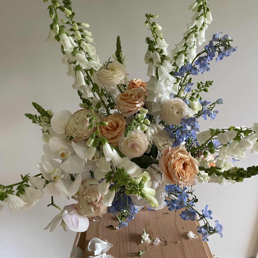 A large beautiful bouquet with several different flowers and greenery in shades of white, blush, cream, and light blue.