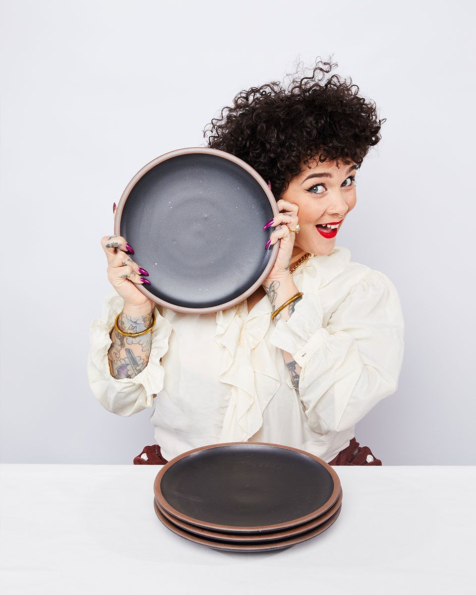 A person is smiling holding up a ceramic black dinner plate to their face.