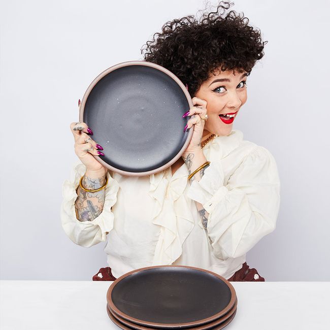 A person is smiling holding up a ceramic black dinner plate to their face.