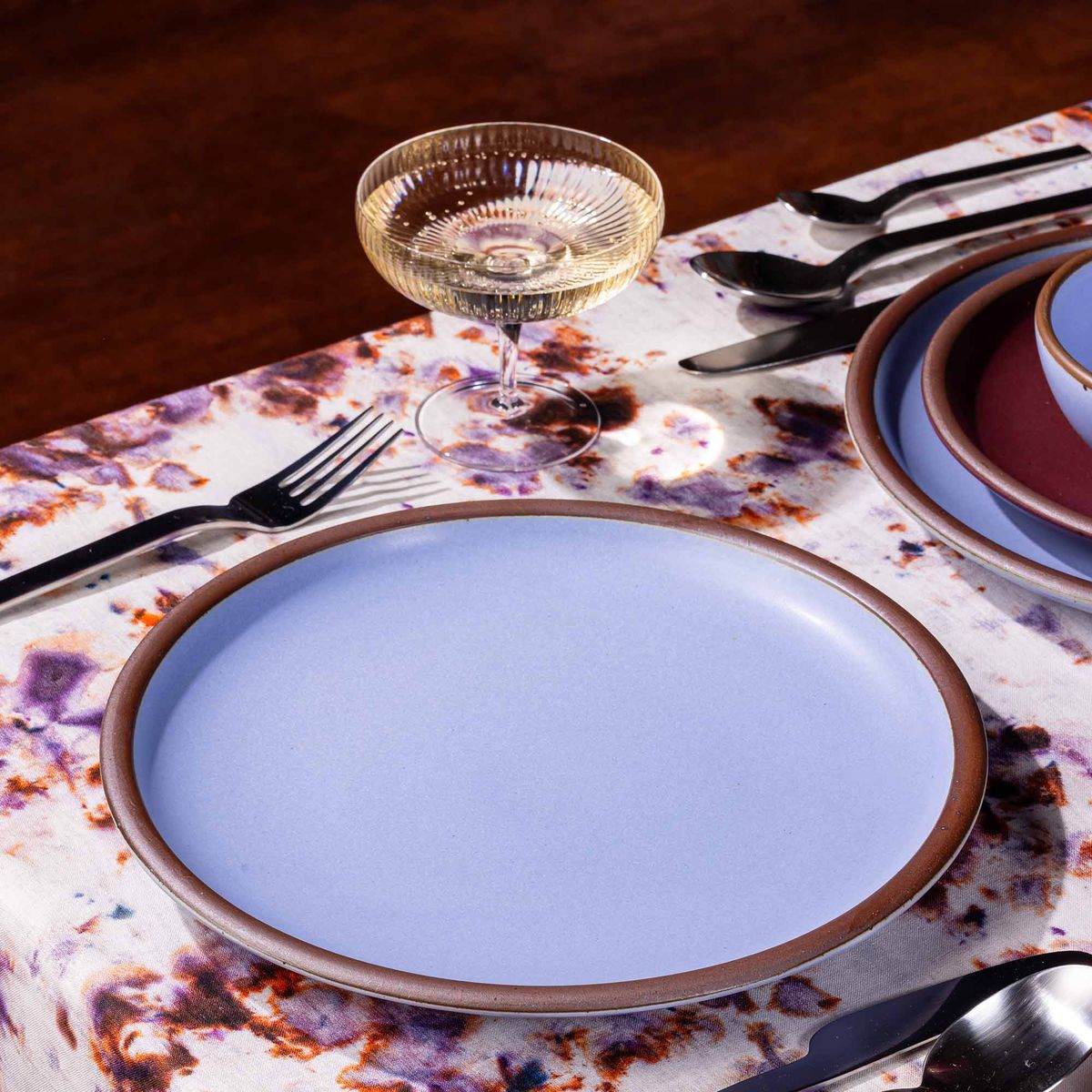 A table setting featuring marbled textiles, a coupe glass, and a dinner plates in periwinkle