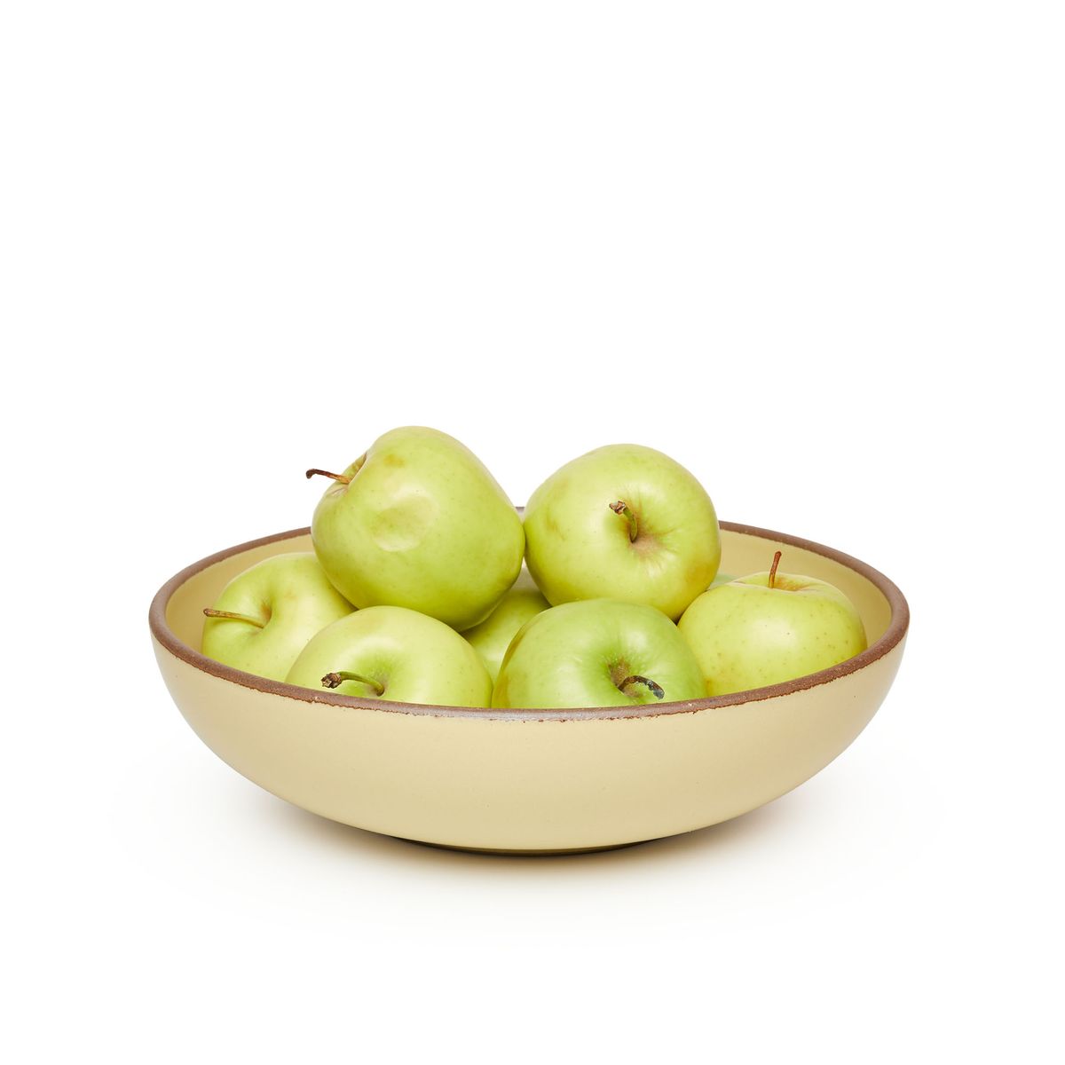 A large shallow serving ceramic bowl in a light butter yellow color featuring iron speckles and an unglazed rim, filled with apples