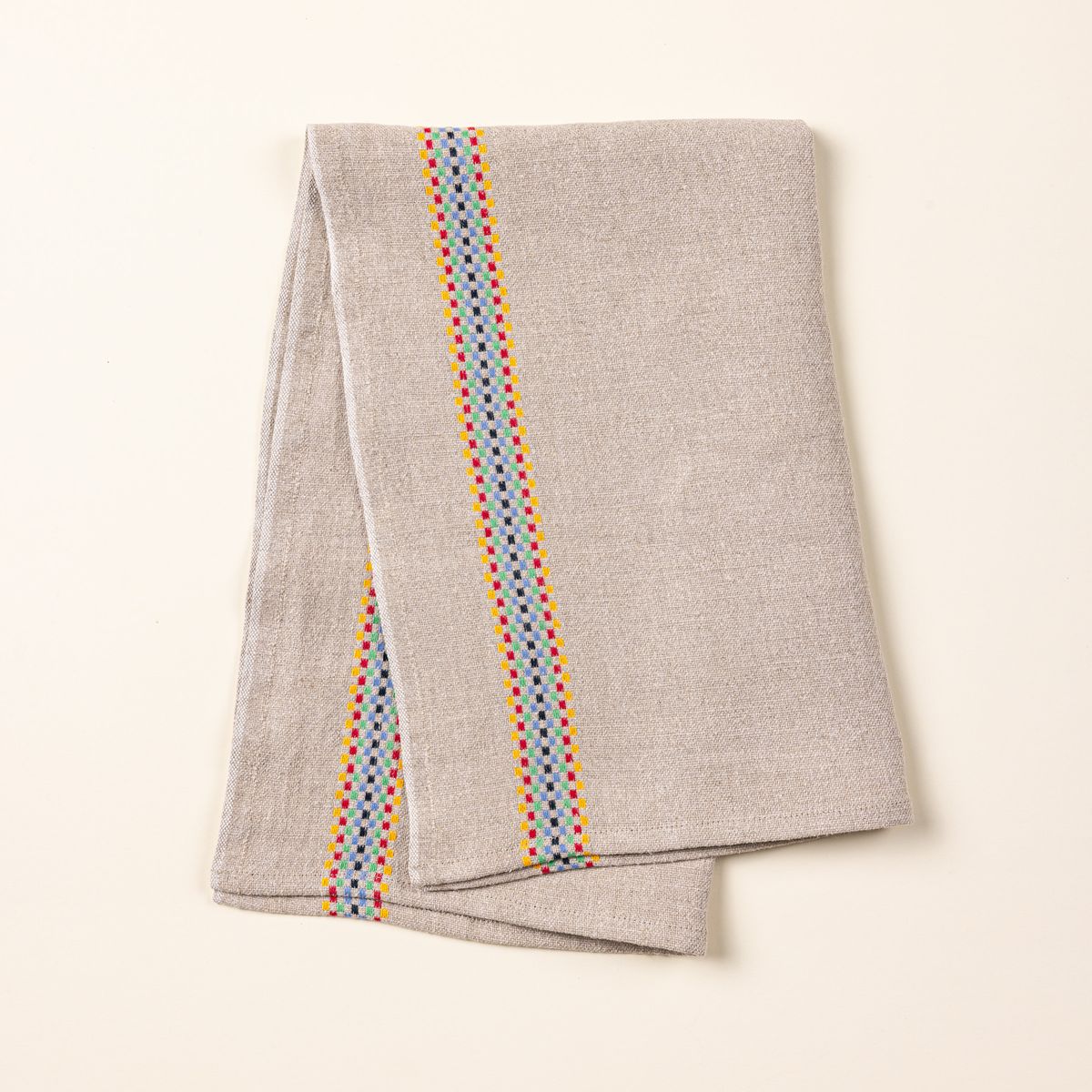 A folded linen towel in a beige color with a multicolor checkerboard stripe down the side