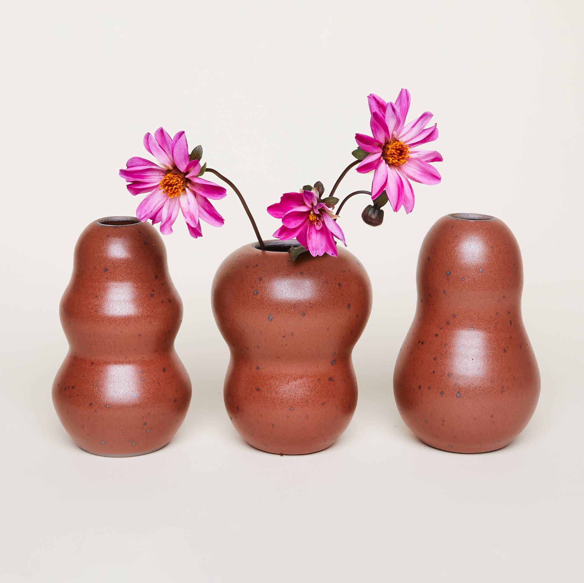 Three curvy ceramic flower vases in a cool terracotta color with flowers inside the middle one.
