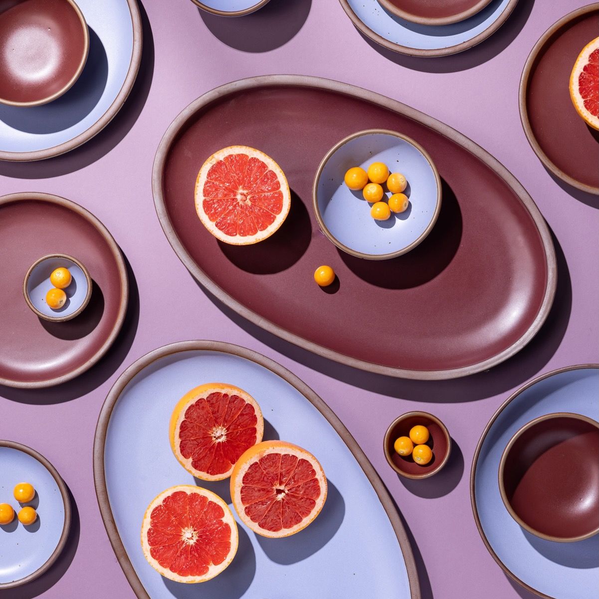 An artful layout of ceramic dishes in periwinkle and plum including oval platters with grapefruit.