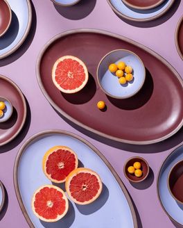 An artful layout of ceramic dishes in periwinkle and plum including oval platters with grapefruit.