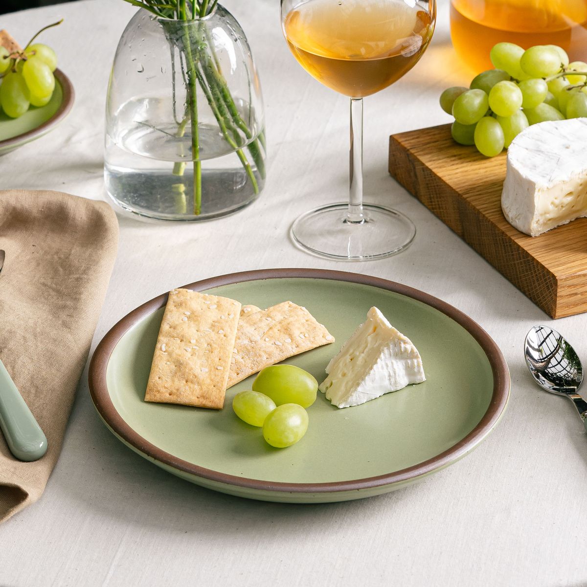 A medium sized calming sage green plate with crackers, grapes and cheese in a table setting.