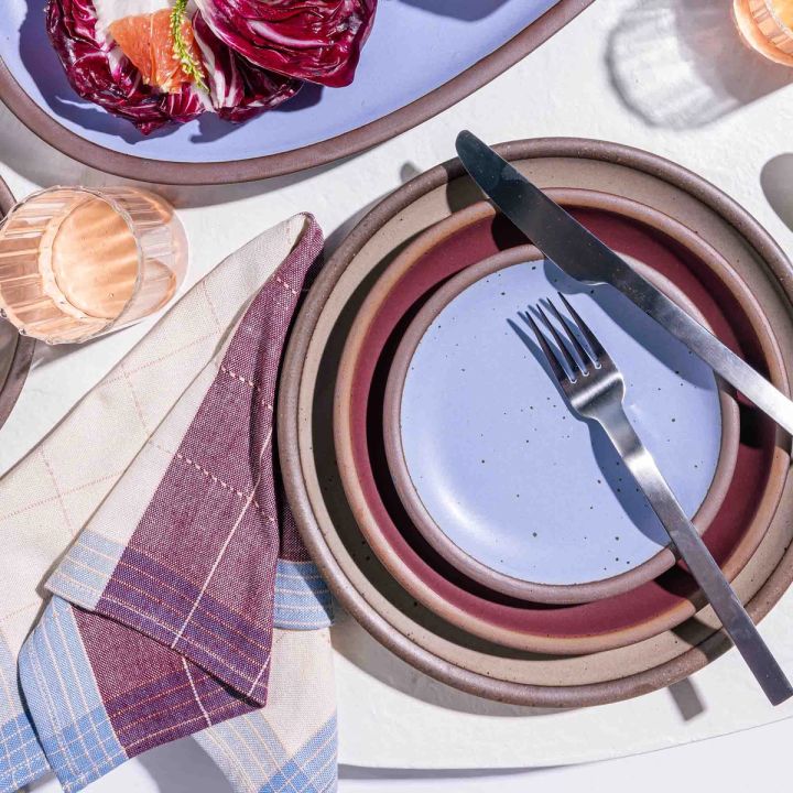 An overhead view of a place setting with dishes in periwinkle and plum colors, with a matching plaid napkin.