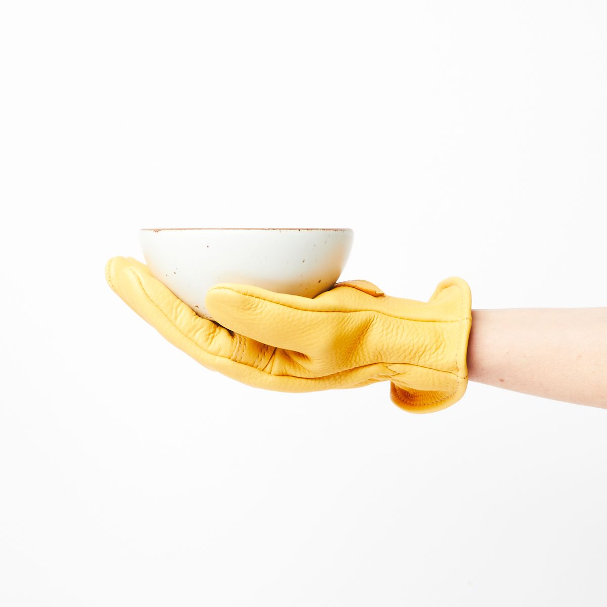 A hand wearing a buttery yellow deerskin garden gloves holding a cool white bowl