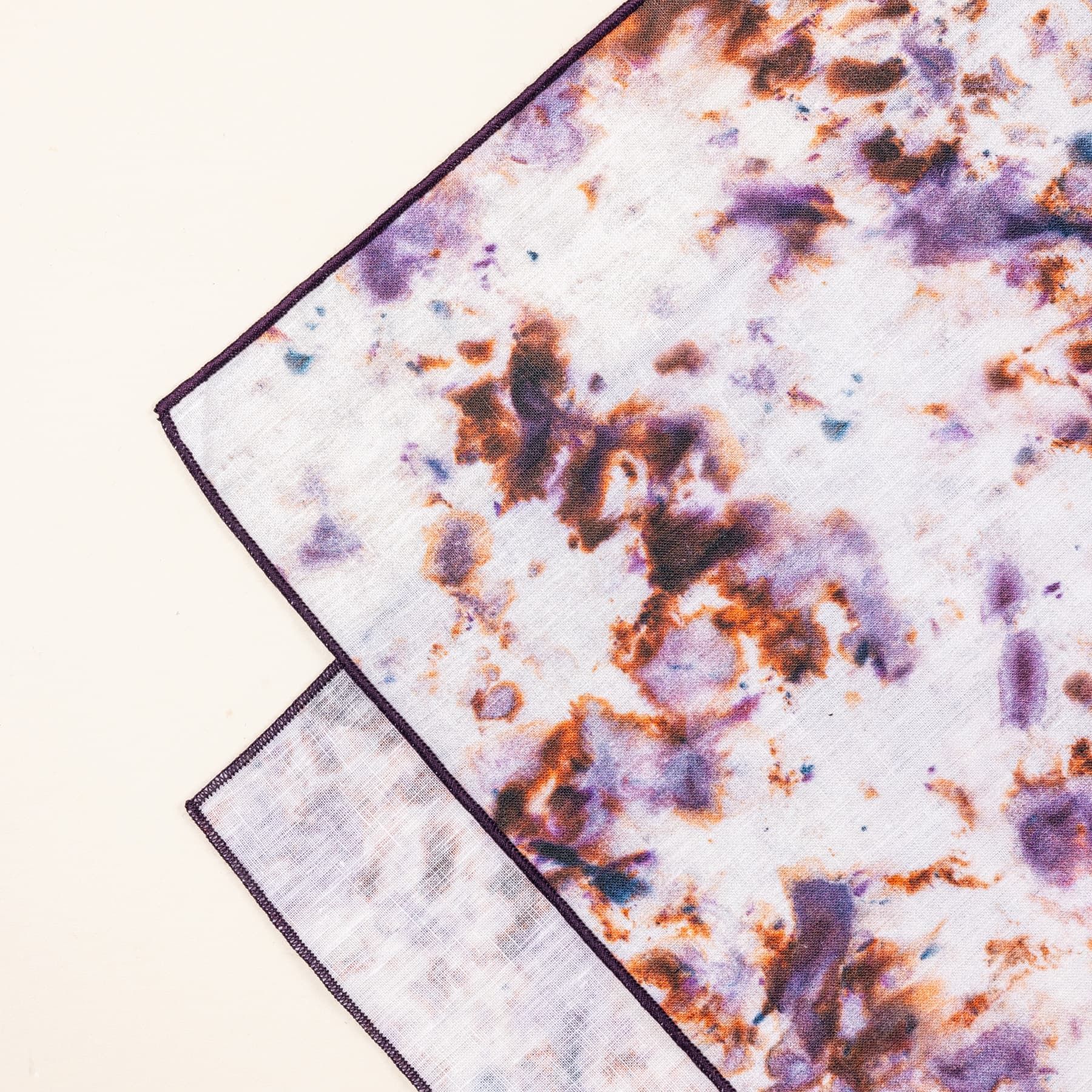 A close up of a corner of a table runner with a marble pattern featuring pink, purple, orange and white colors folded artfully