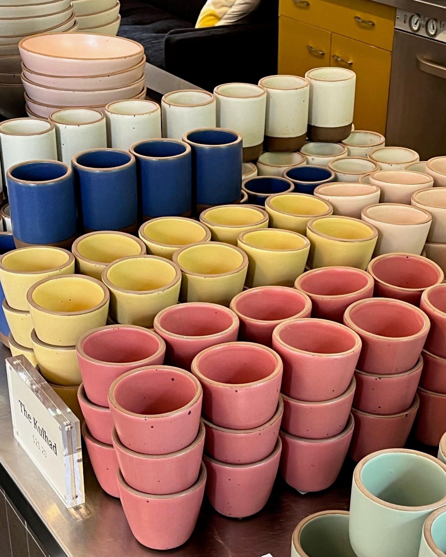 In a retail setting, there are large stacks of ceramic cups and mugs in all different colors of the rainbow