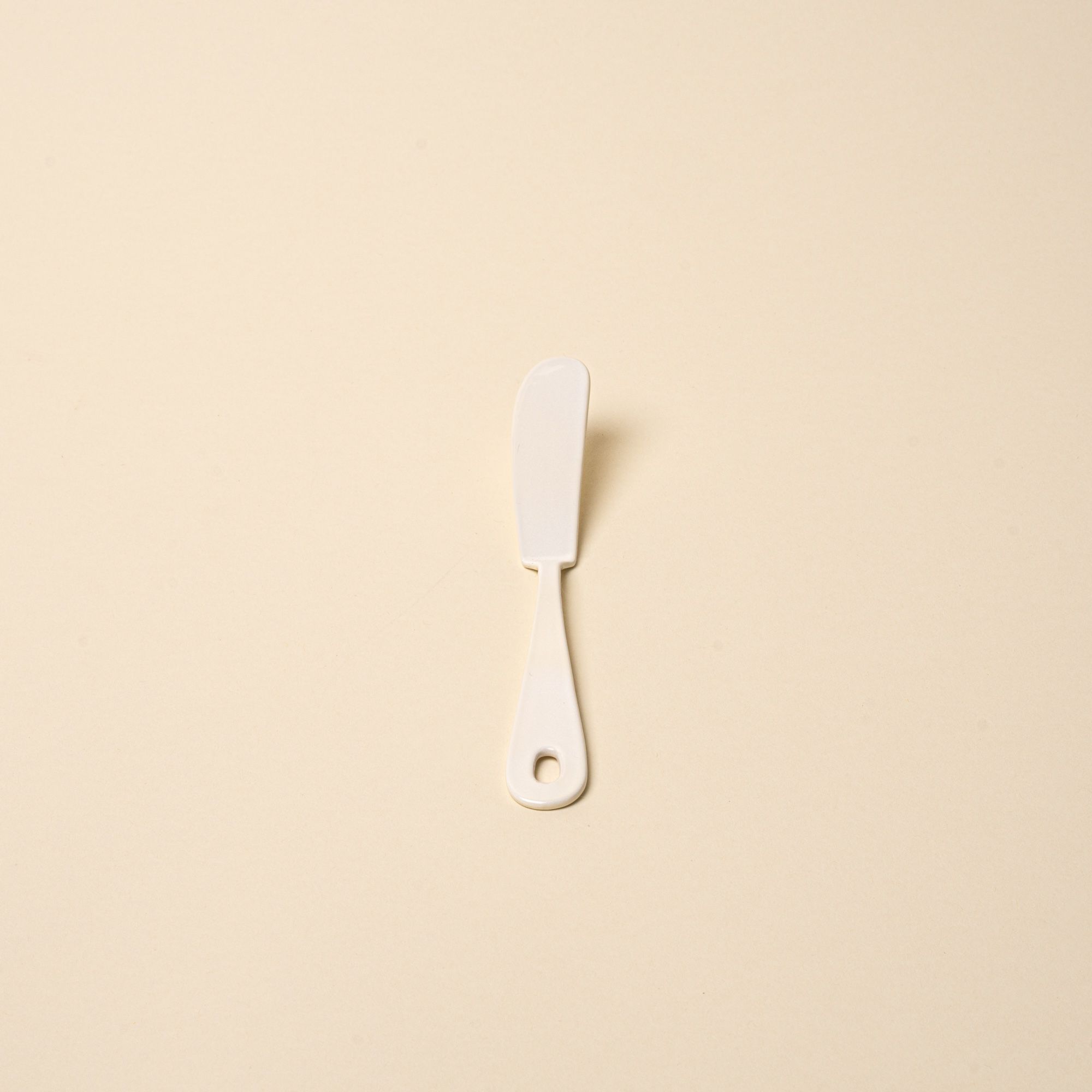 A white enamel butter knife with a hole at the end of the handle.