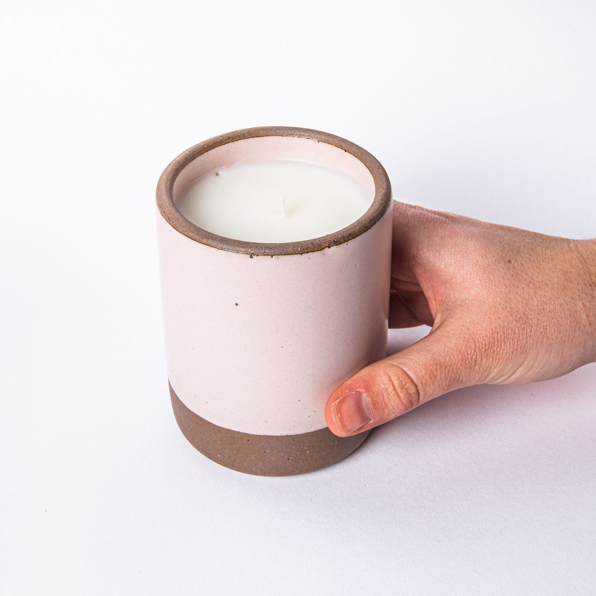 Hand holding a large ceramic vessel in soft light pink color with candle inside