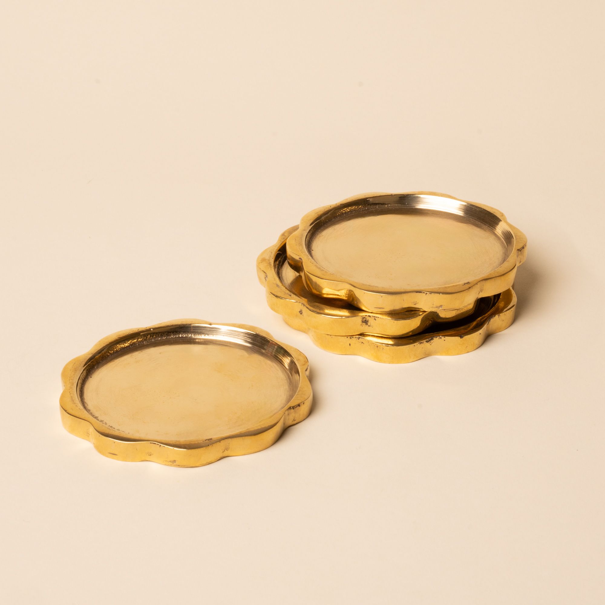 Set of round gold-toned coasters with scalloped edges, stacked neatly on a light surface.