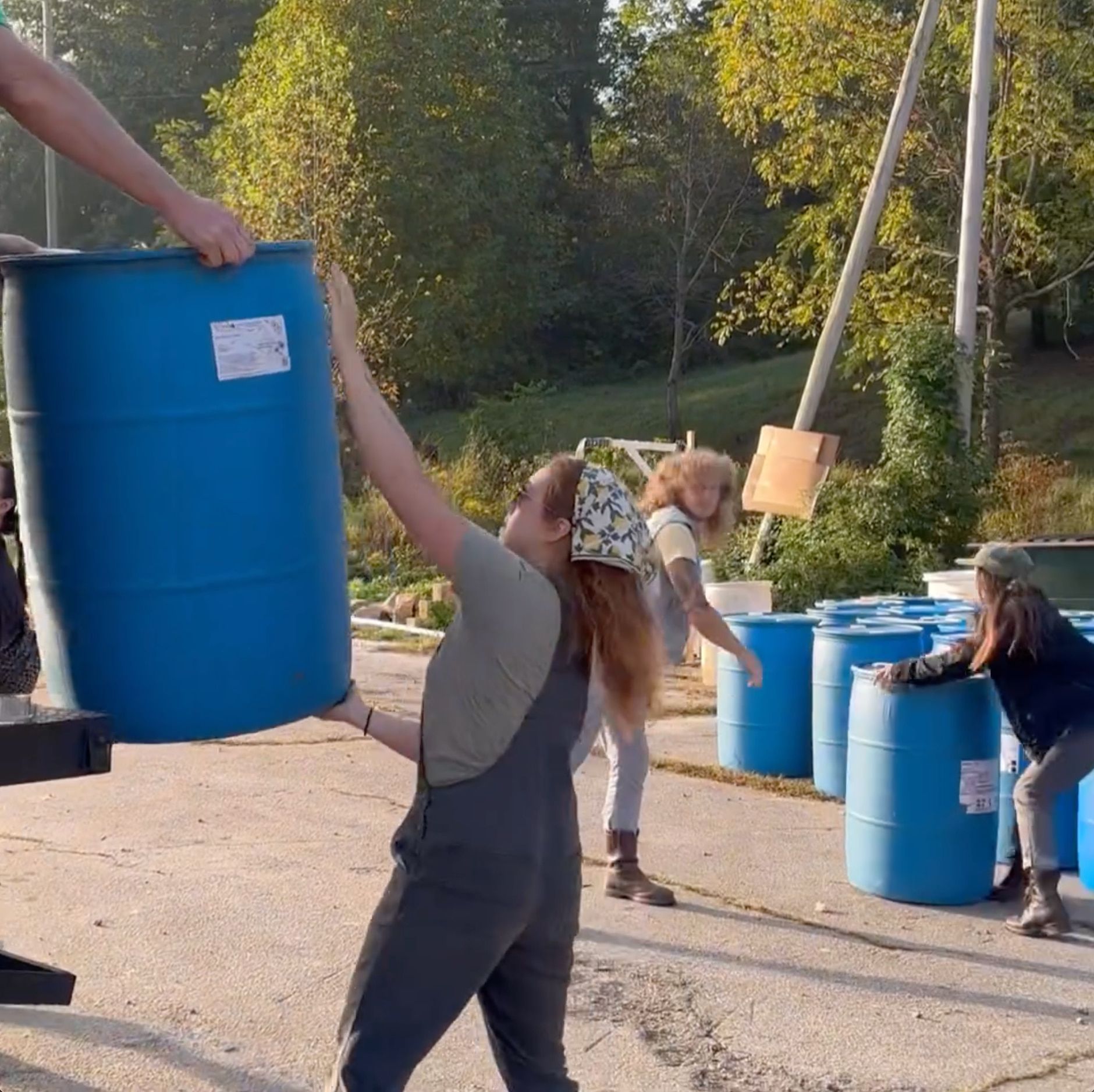 A person is grabbing a barrel of water from someone. There are barrels of water in the background.