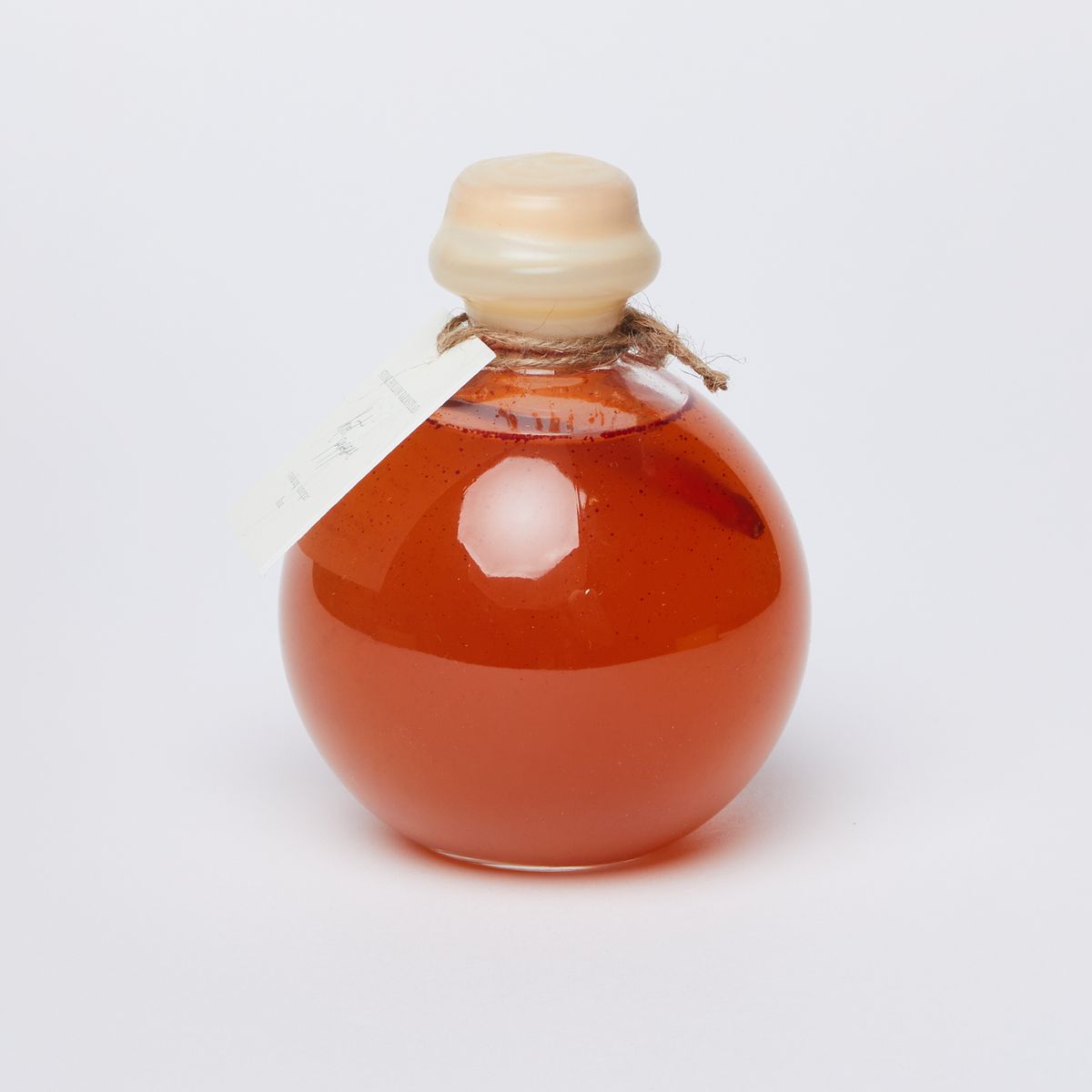 A clear spherical bottle full of a red liquid with a cork covered in wax and a white label tied with string around the neck