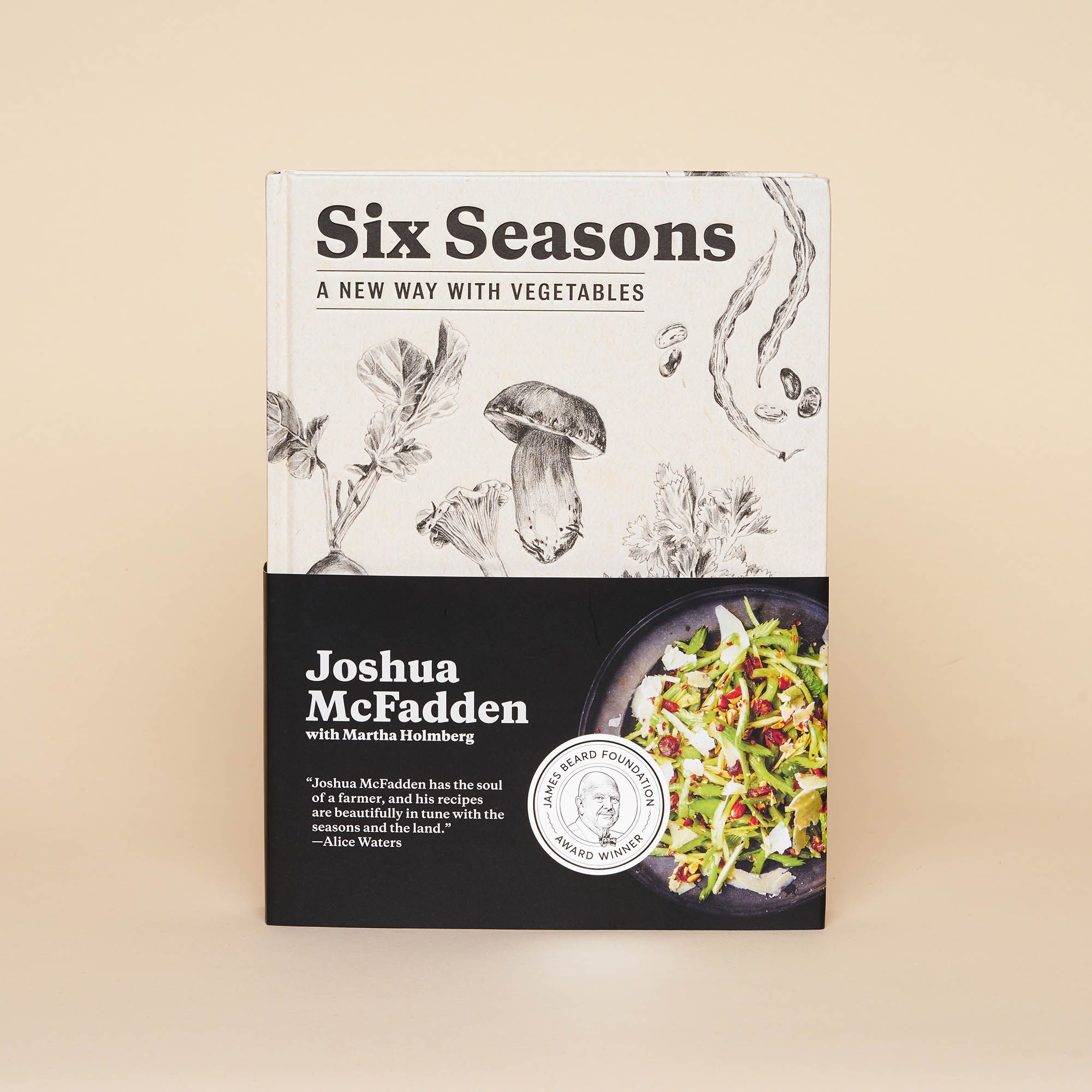 An off-white cookbook with delicate illustrations of beets, onions, mushrooms, green beans and celery. A half-book size removable sleeve is over the book, showing a colorful salad and James Beard Award Winner stamp.