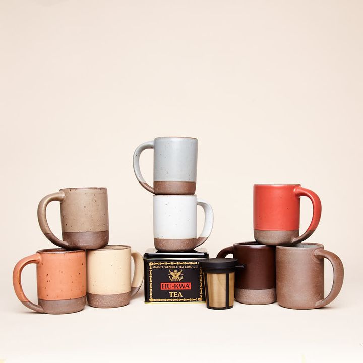 Hu-Kwa Tea in a black tin, alongside a brewing basket and an assormtnet of East Fork Mugs