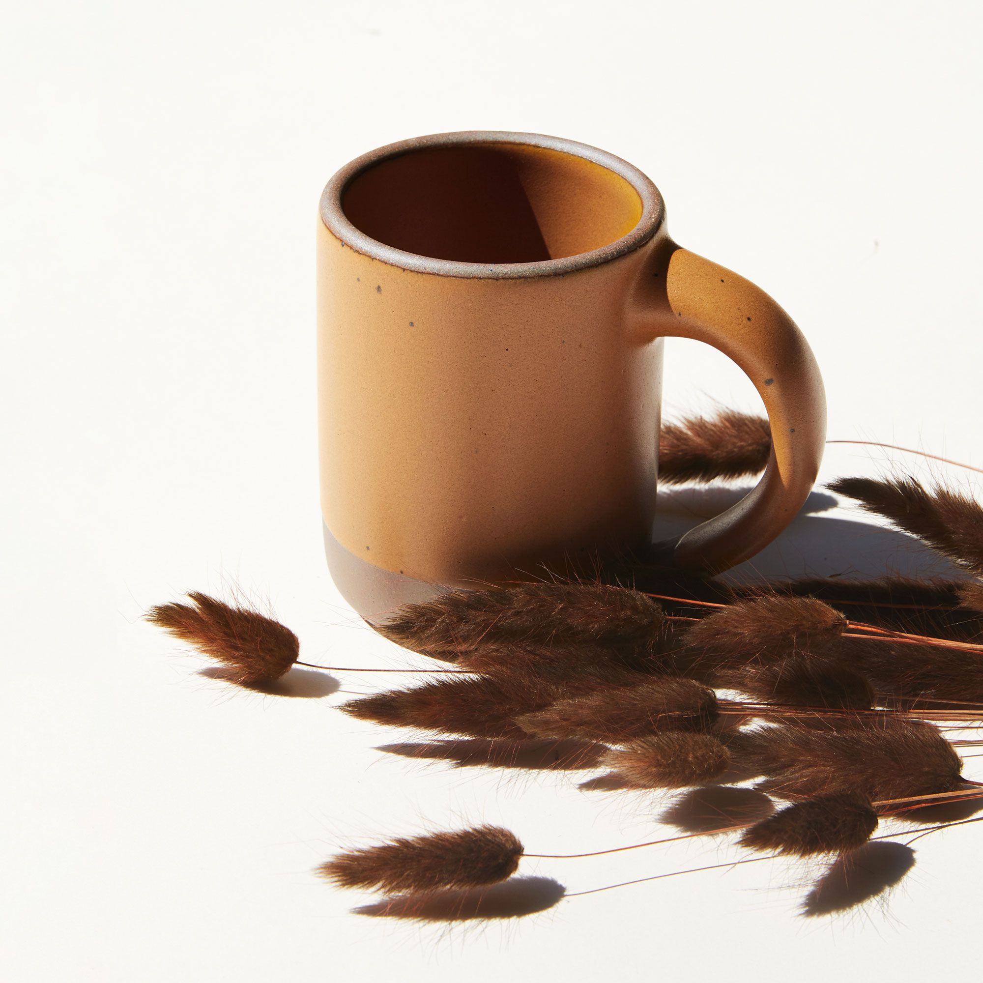 A ceramic East Fork Mug in a dark gold color with dried bunny tail grass in a darker hue.