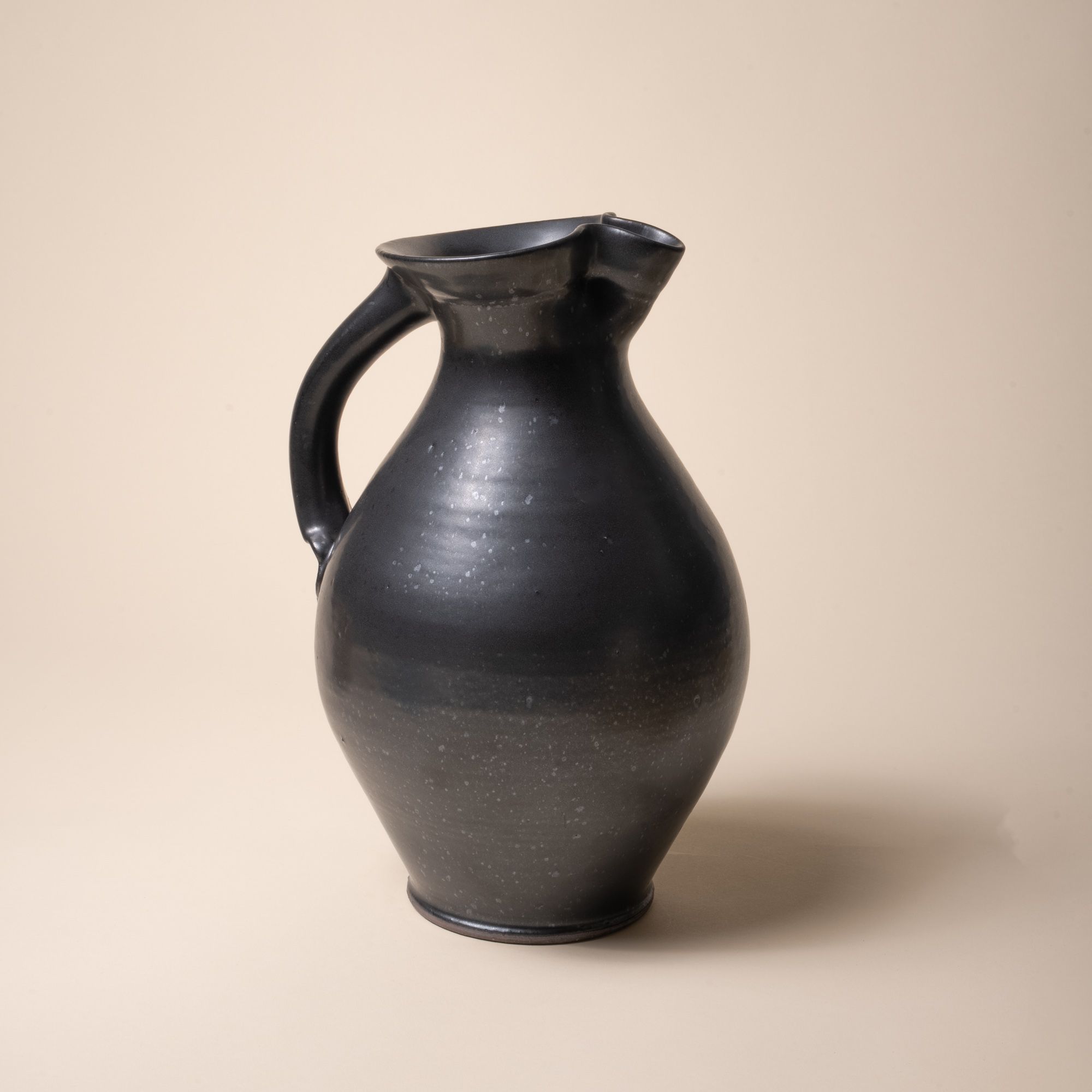 A hand-formed large classic ceramic pitcher with a spout and handle in a black graphite color with iron speckles