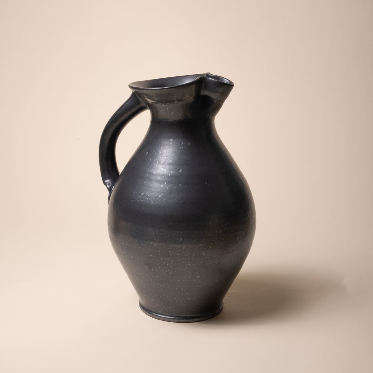 A hand-formed large classic ceramic pitcher with a spout and handle in a black graphite color with iron speckles