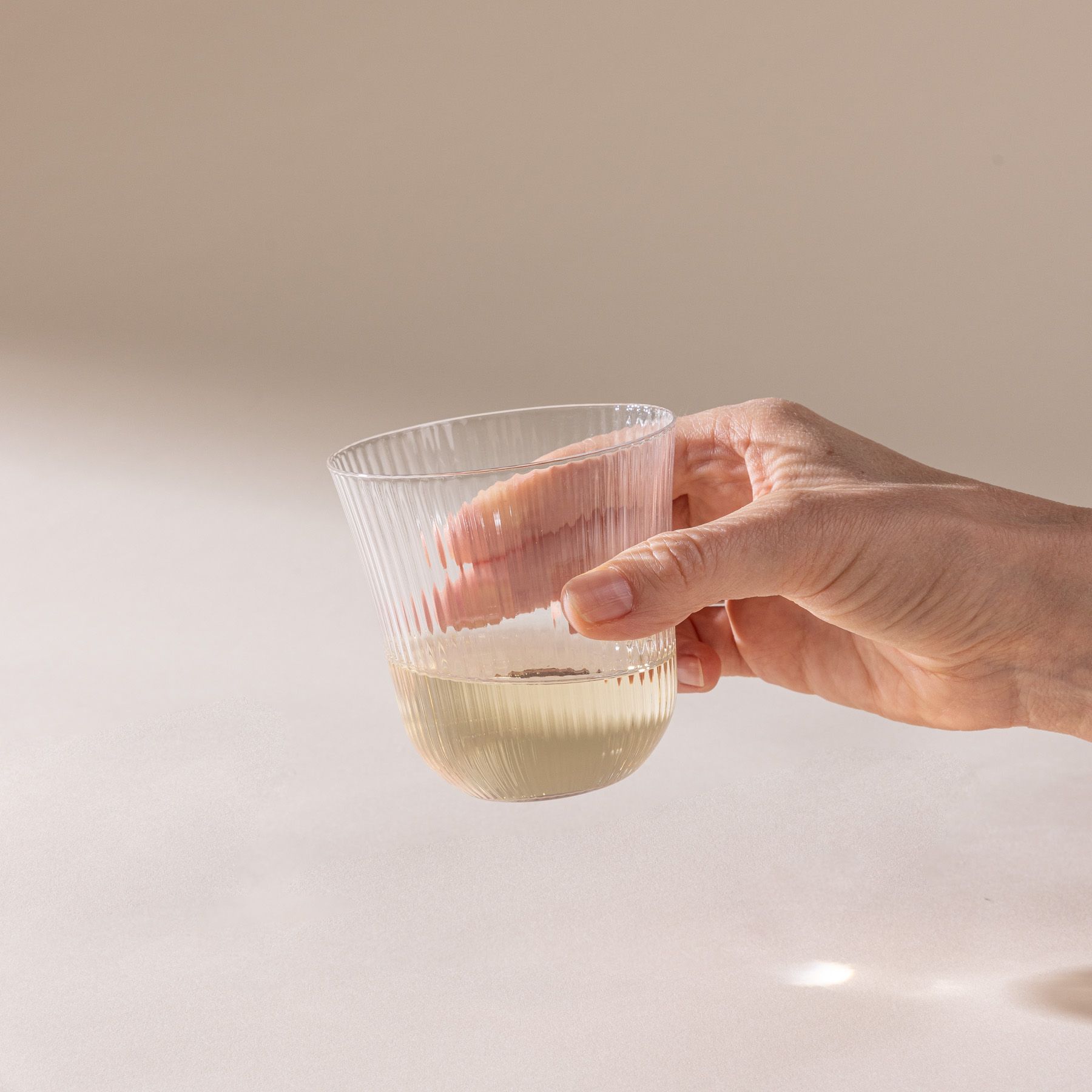 A hand holds a delicate ribbed glass that has a rounded curve on the bottom and curves out on the top, filled with champagne.