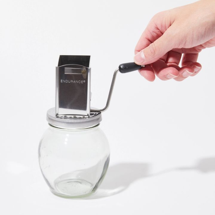 Square metal shute with a S-curved crank handle atop a clear round glass jar