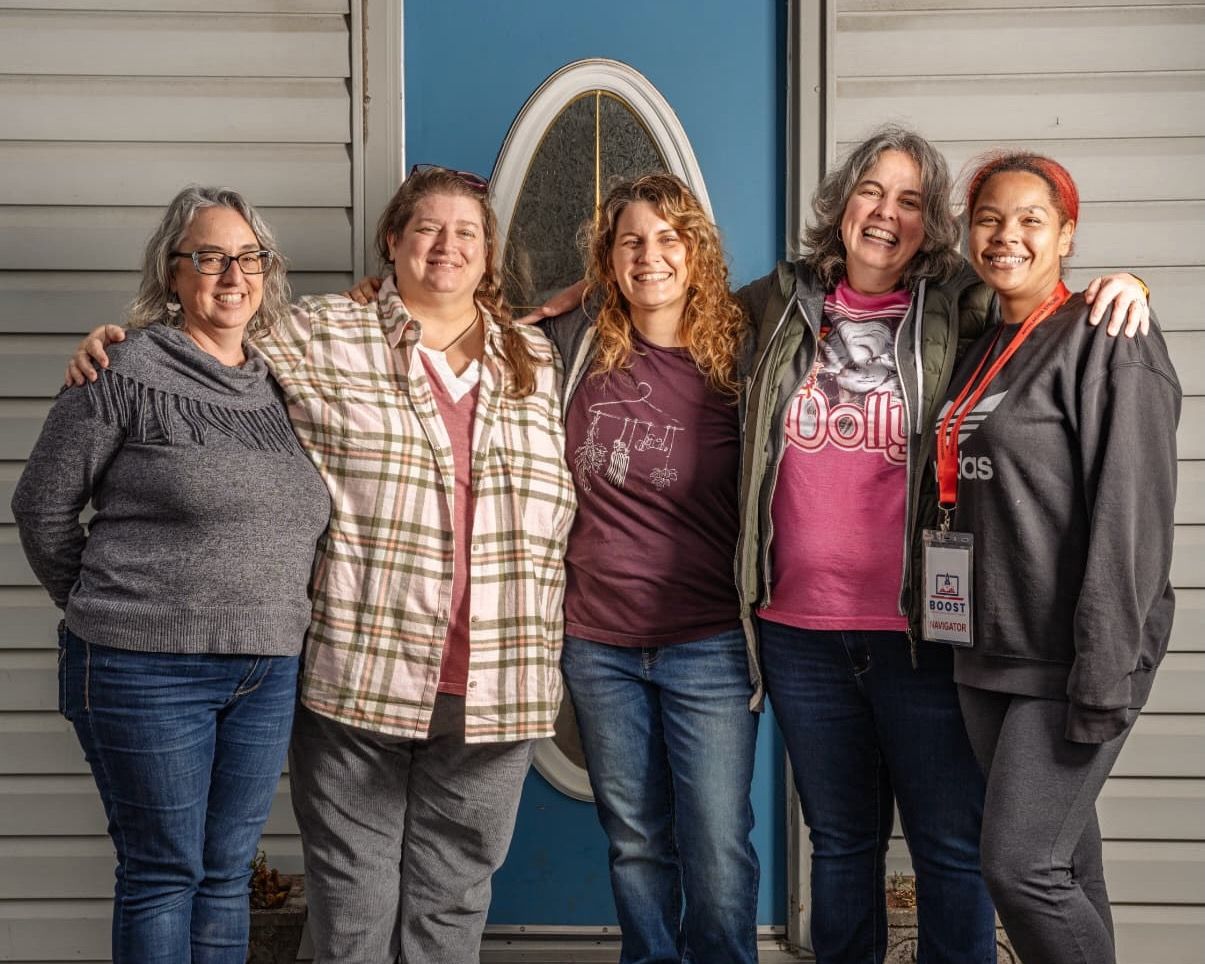 Five people gather together smiling in front of a building with a blue door.