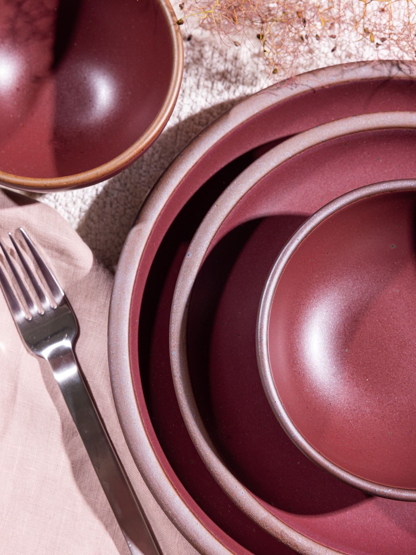 Ceramic dinnerware in a deep plum color place setting with light napkin and metallic fork.