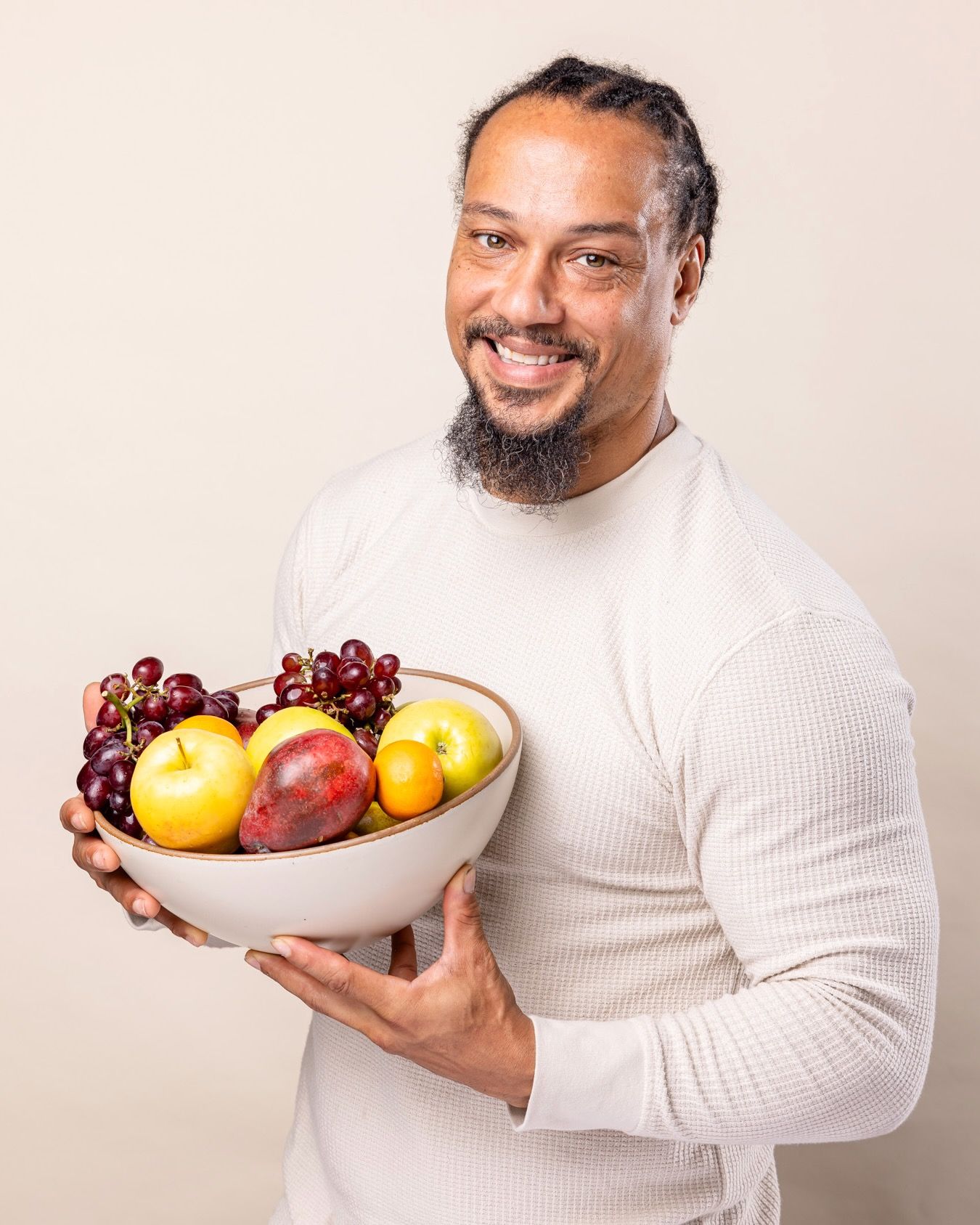 A man is smiling and holding a large ceramic cream bowl of whole fruit
