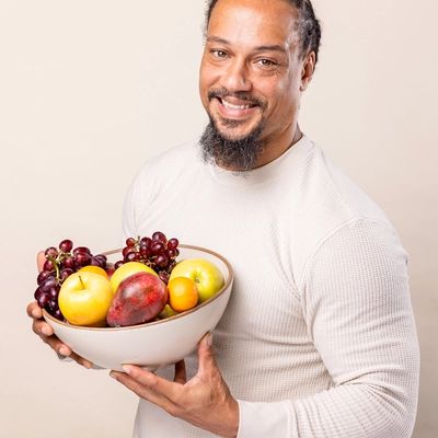 A man is smiling and holding a large ceramic cream bowl of whole fruit