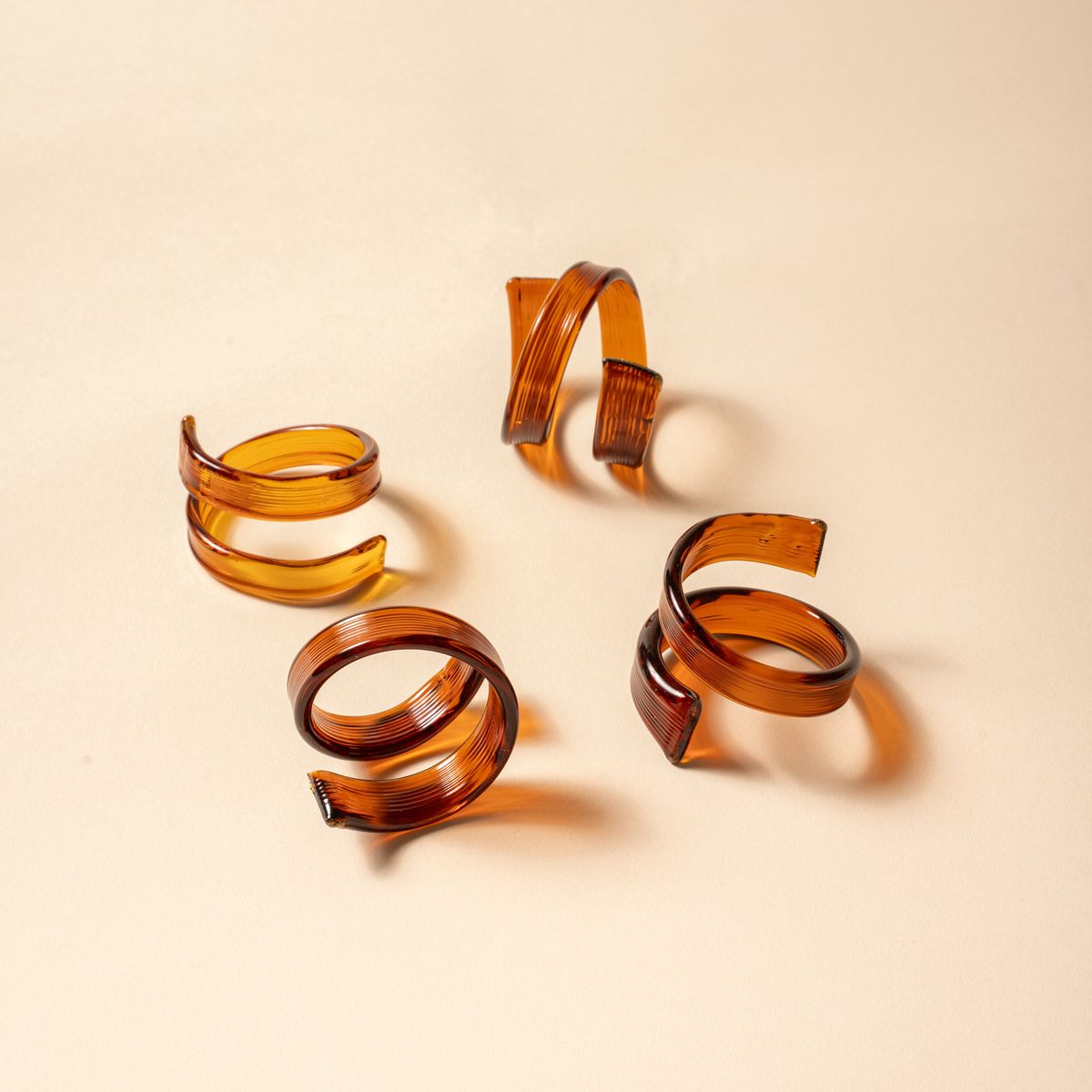 Set of four amber glass napkin rings with a coiled, ribbon-like design on a neutral background.