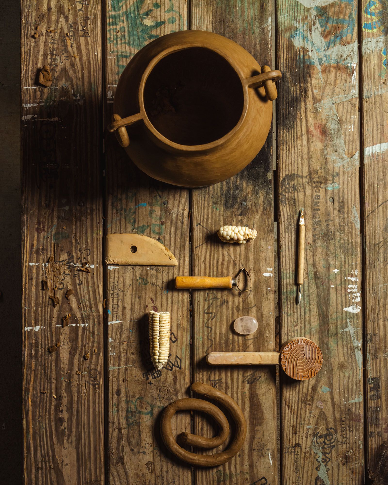 An overhead view of pottery tools, pencil, and clay next to a finished formed clay pot.