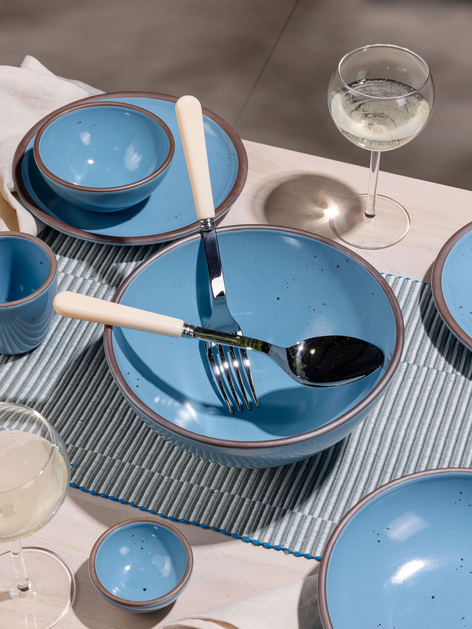 A large fork and spoon with cream handles sit inside a ceramic bowl in a robin's egg blue color. Other bowls of various sizes surround.