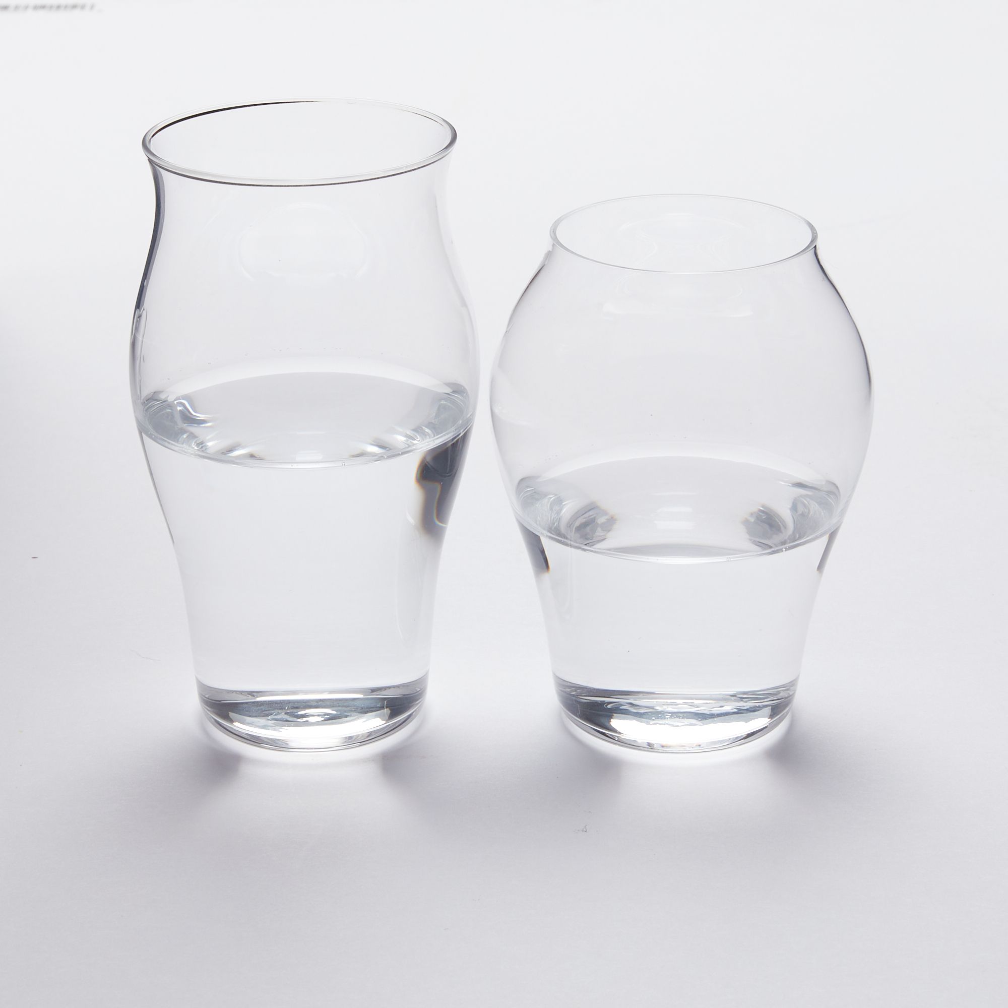 Two clear glasses filled halfway with water, one taller than the other, both with curved bodies.