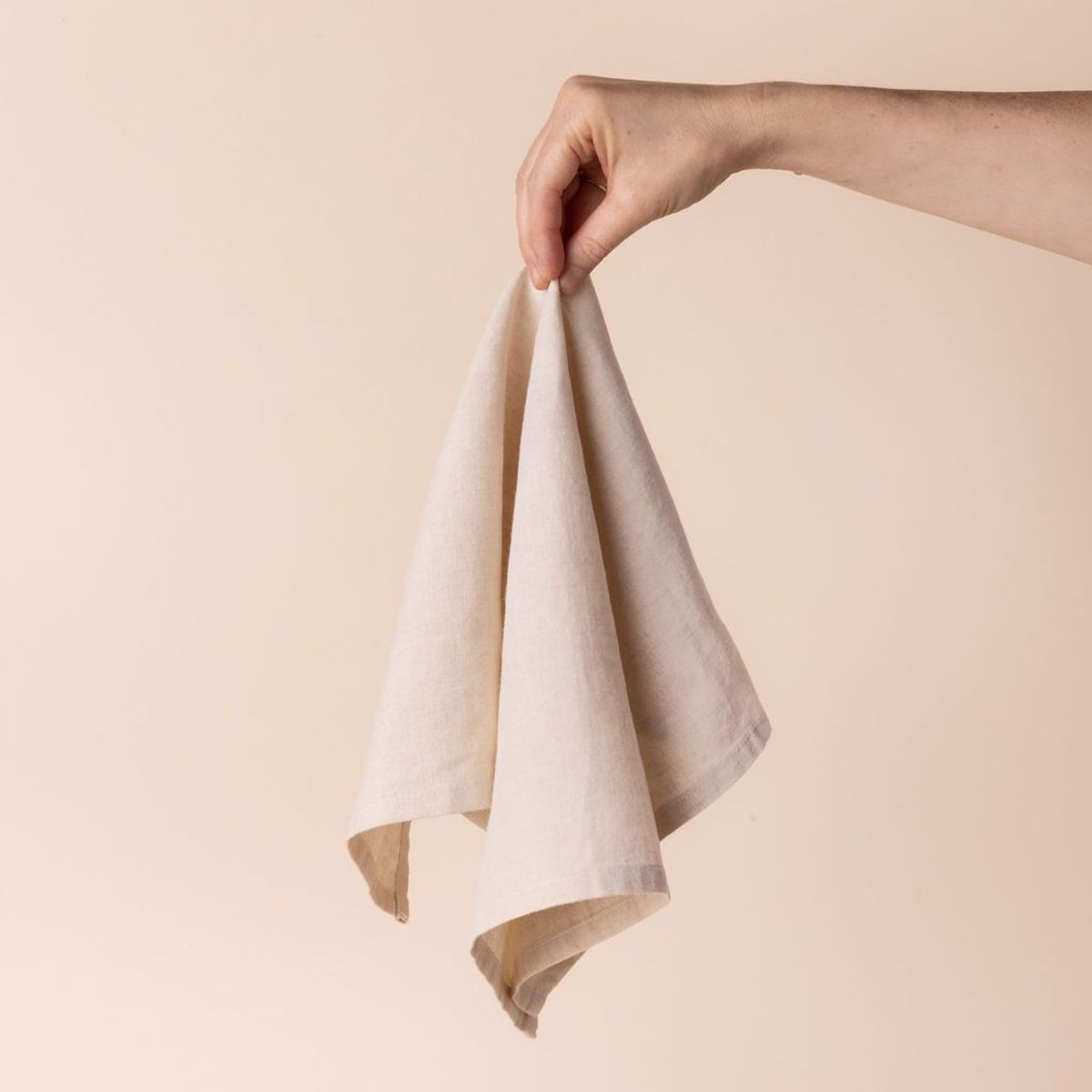 Hand holding a linen napkin in an off-white color from the center 