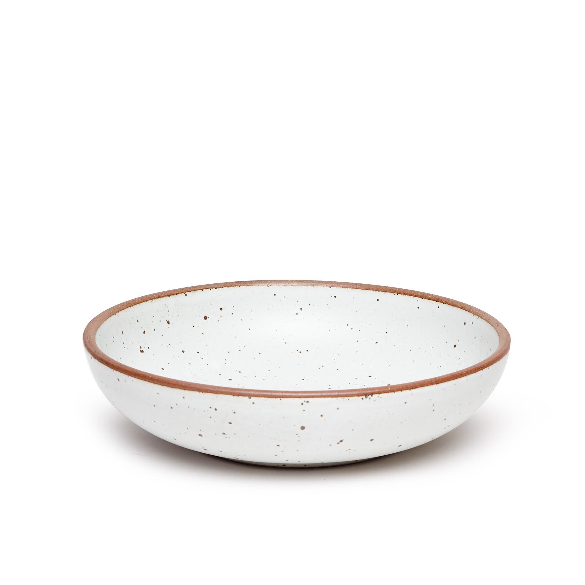 A large shallow serving ceramic bowl in a cool white color featuring iron speckles and an unglazed rim.