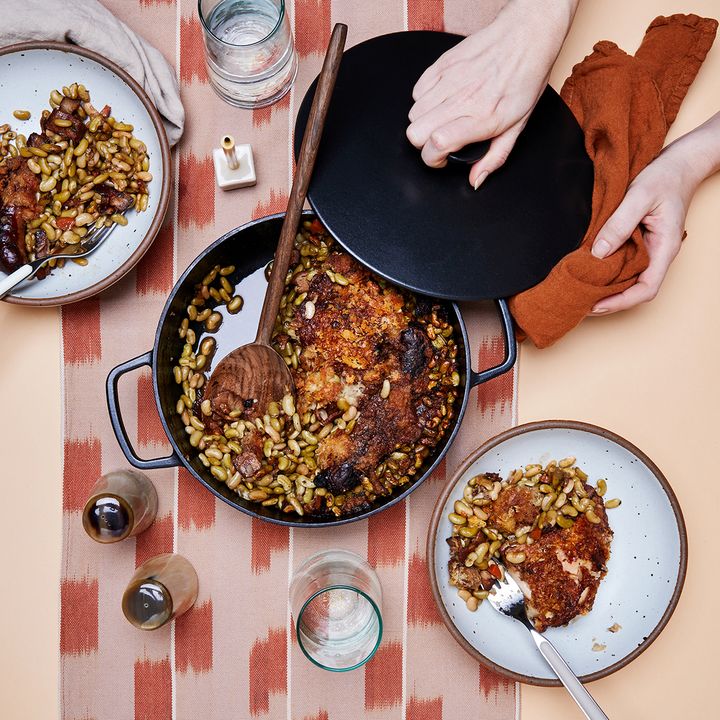 A birds-eye-view of a table with a red patterene table running, bowls, and a center piece of a cast iron pot with a savory bean dish.