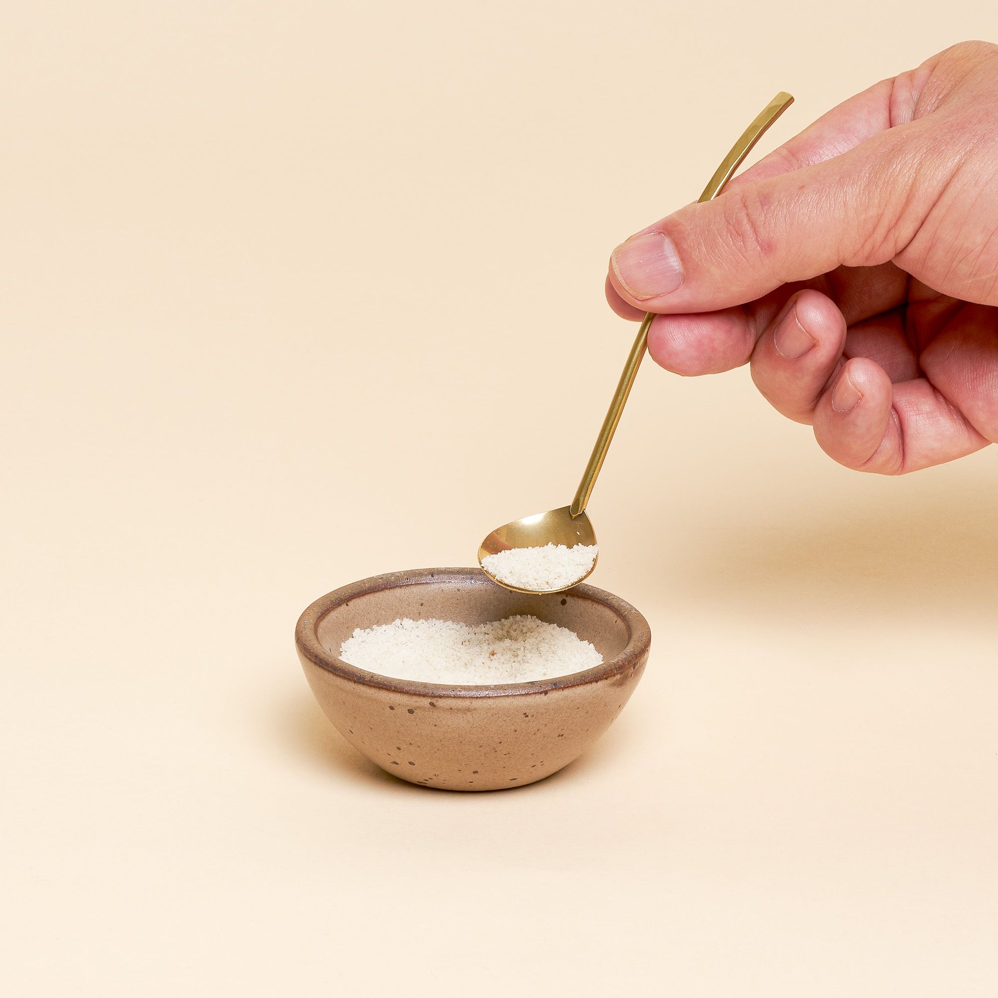 A hand holds a small brass ladle over a Bitty Bowl in Morel filled with sugar