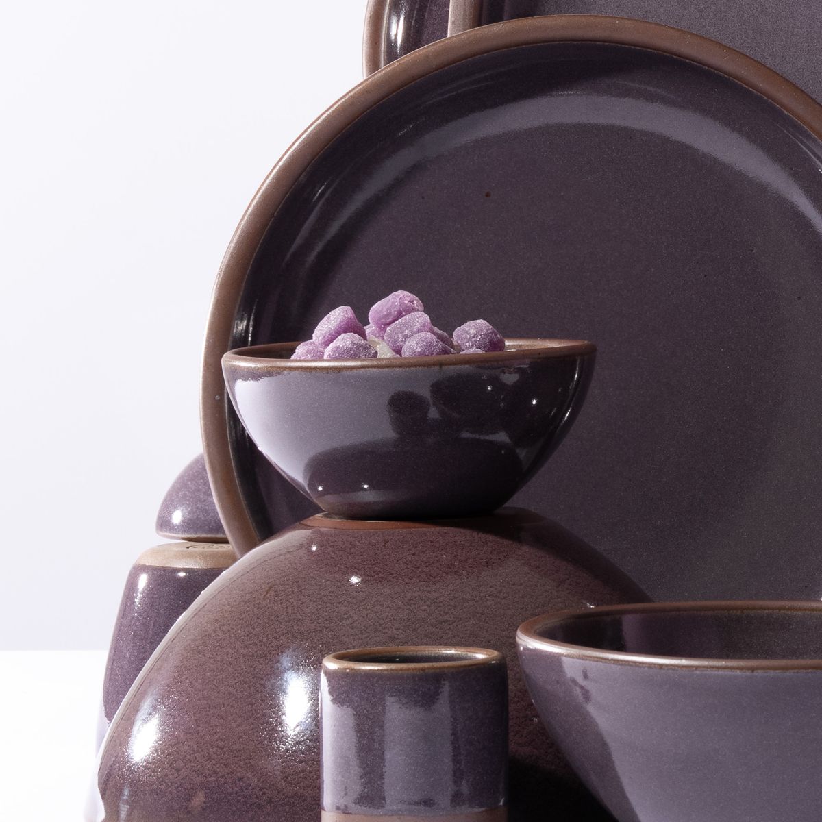 A small dessert bowl in a purple color with a glowing sheen and artfully arranged with other pottery and filled with gumdrops