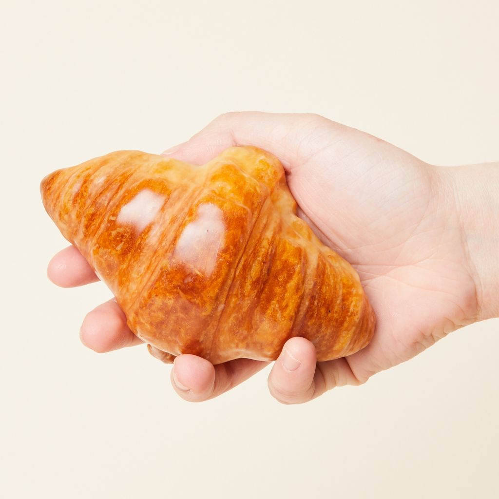 A hand holds a glossy brown object that has the shape and size of a croissant