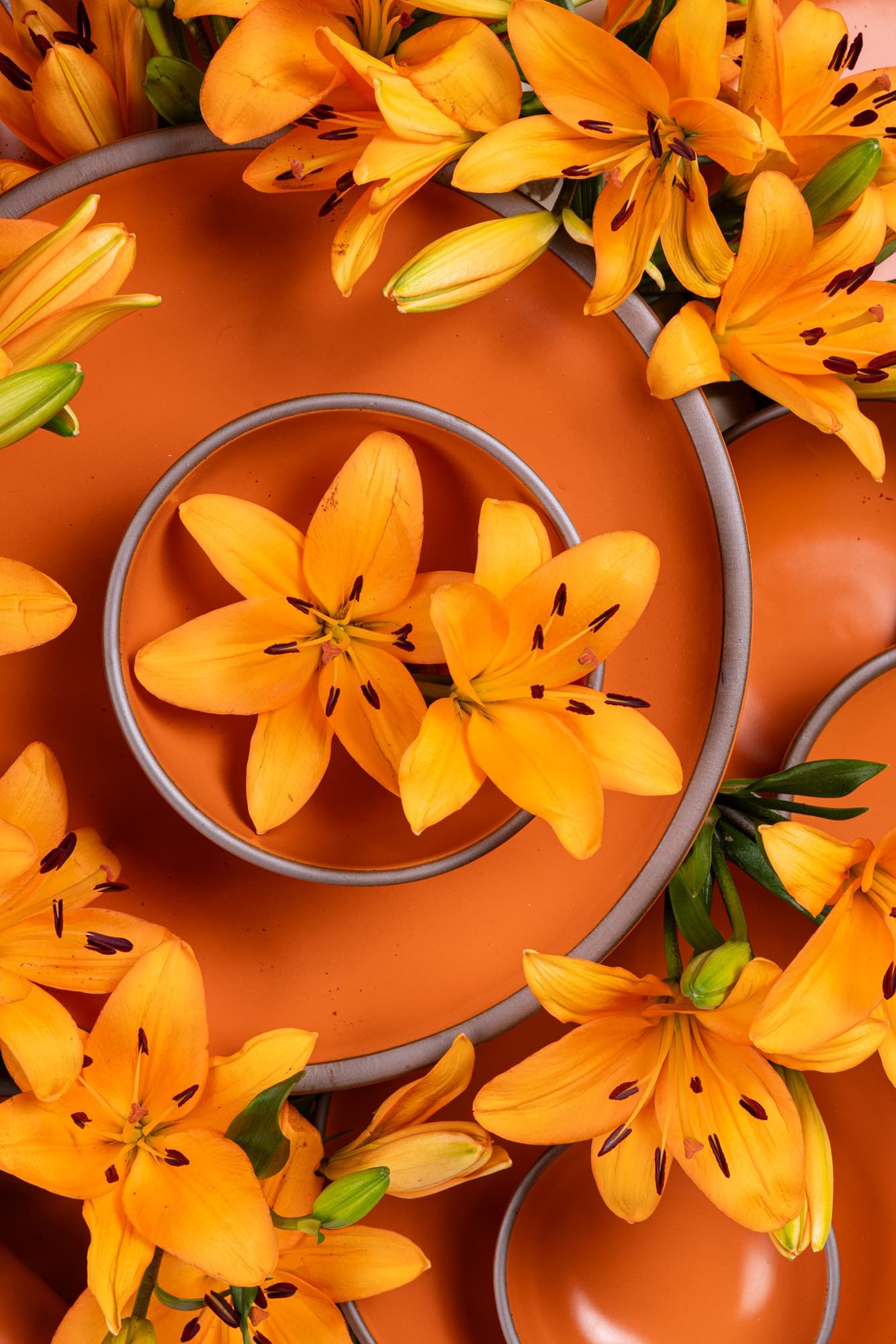 A close up of ceramic bowls and plates stacked together in a bold orange color with daylily flowers everywhere