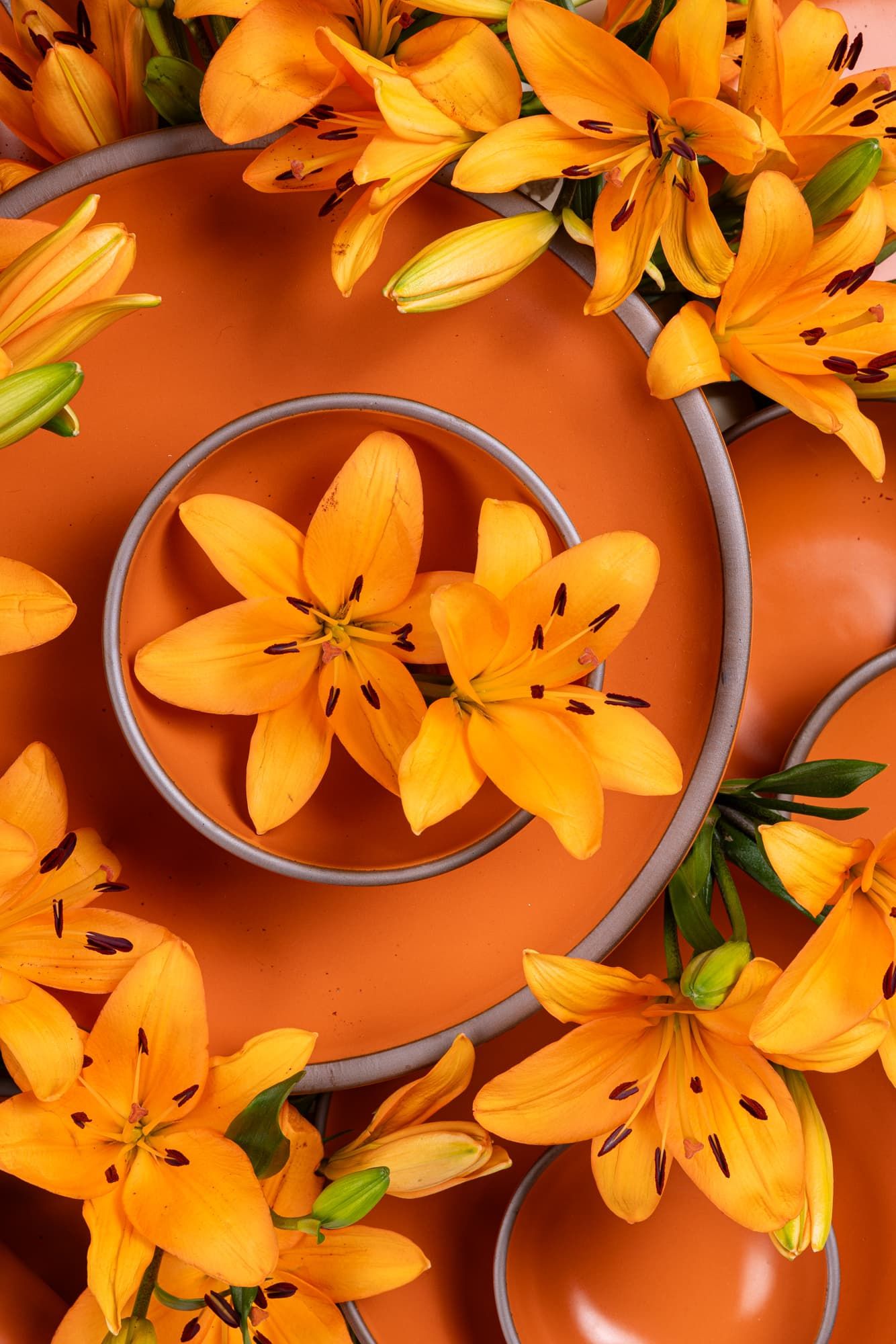 A close up of ceramic bowls and plates stacked together in a bold orange color with daylily flowers everywhere