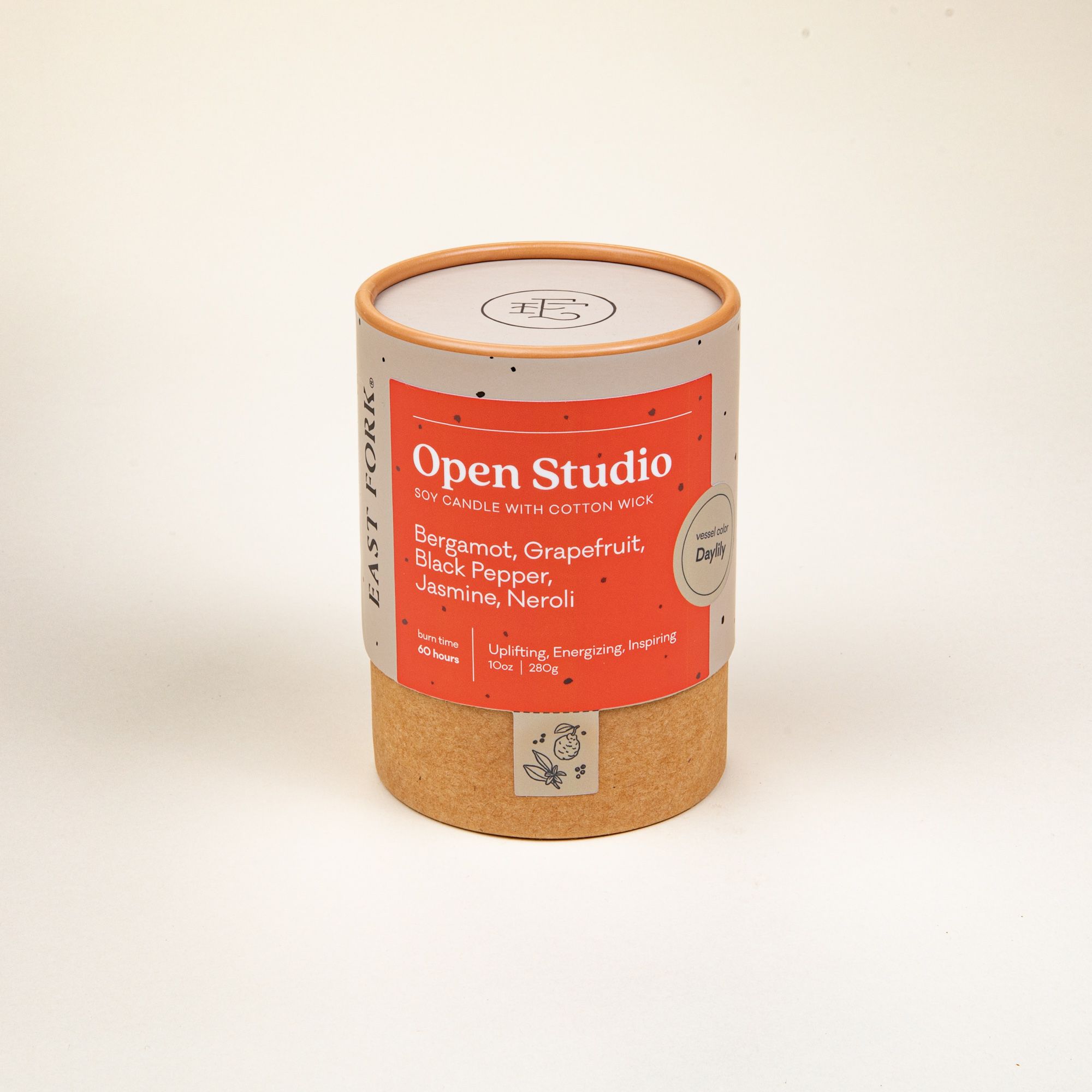 Small cardboard packaging tube with a candle inside with branding on it that says 'Open Studio'