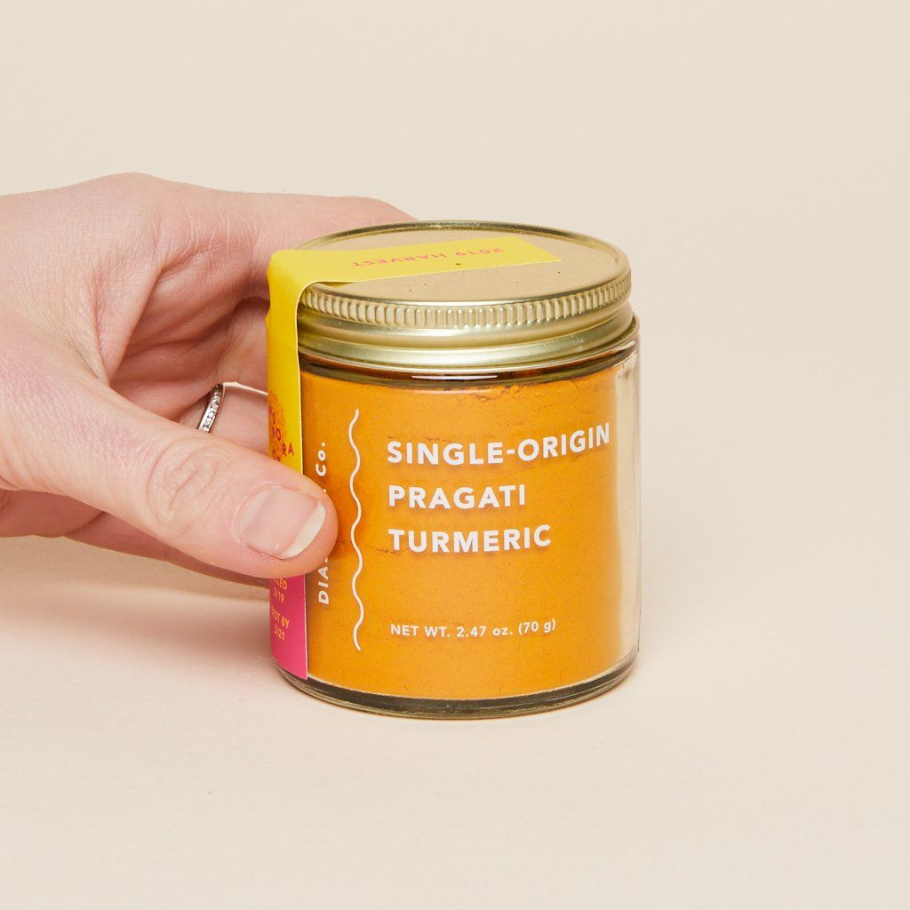 A hand holds a glass jar full of single-origin Pragati turmeric