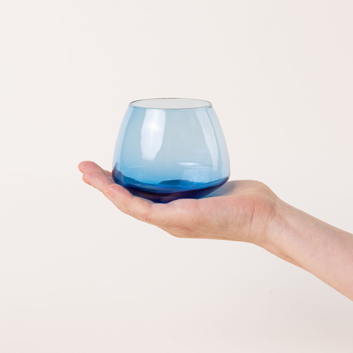 A hand holds a light blue glass whiskey snifter with a rounded base