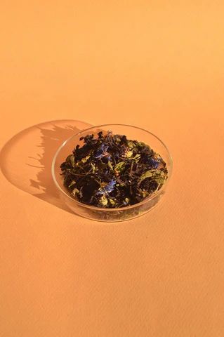 On an orange background, a clear bowl is filled with and herb mix for tea.