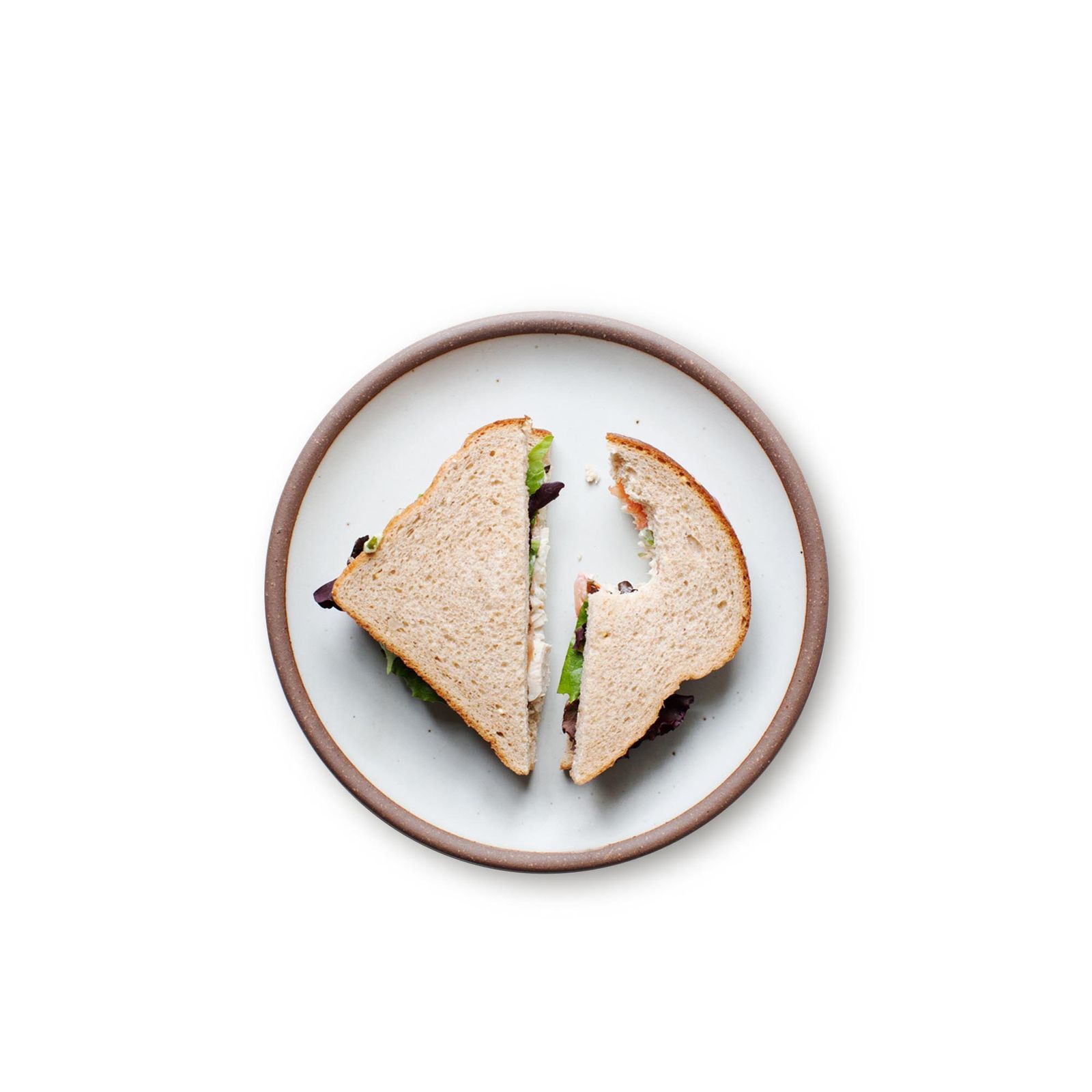 A side plate with a turkey, lettuce, tomato sandwich, cut diagonally, with a bite missing from one half.